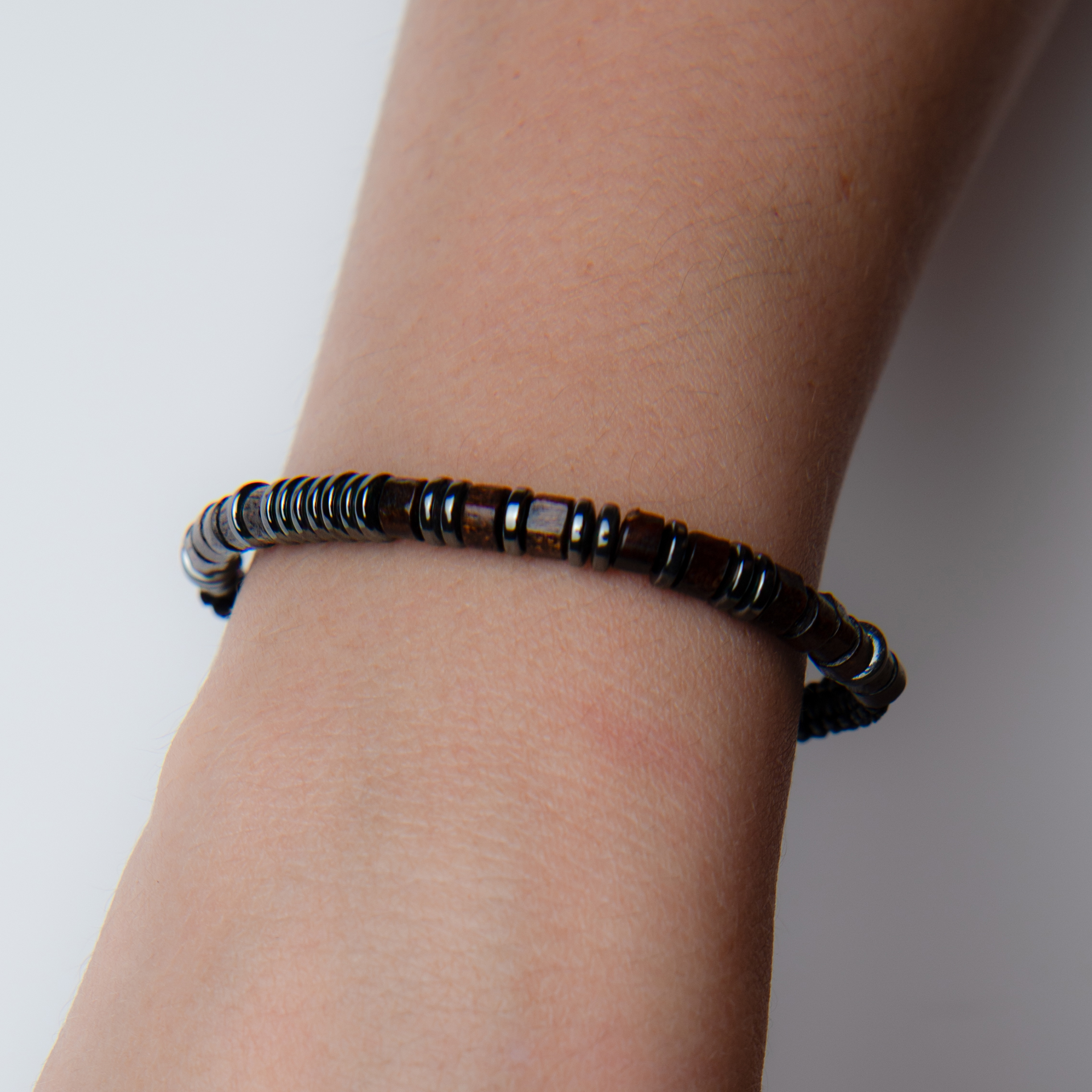 Bracelet image before retouching, showing a dark beaded bracelet worn on the wrist against a soft gray background