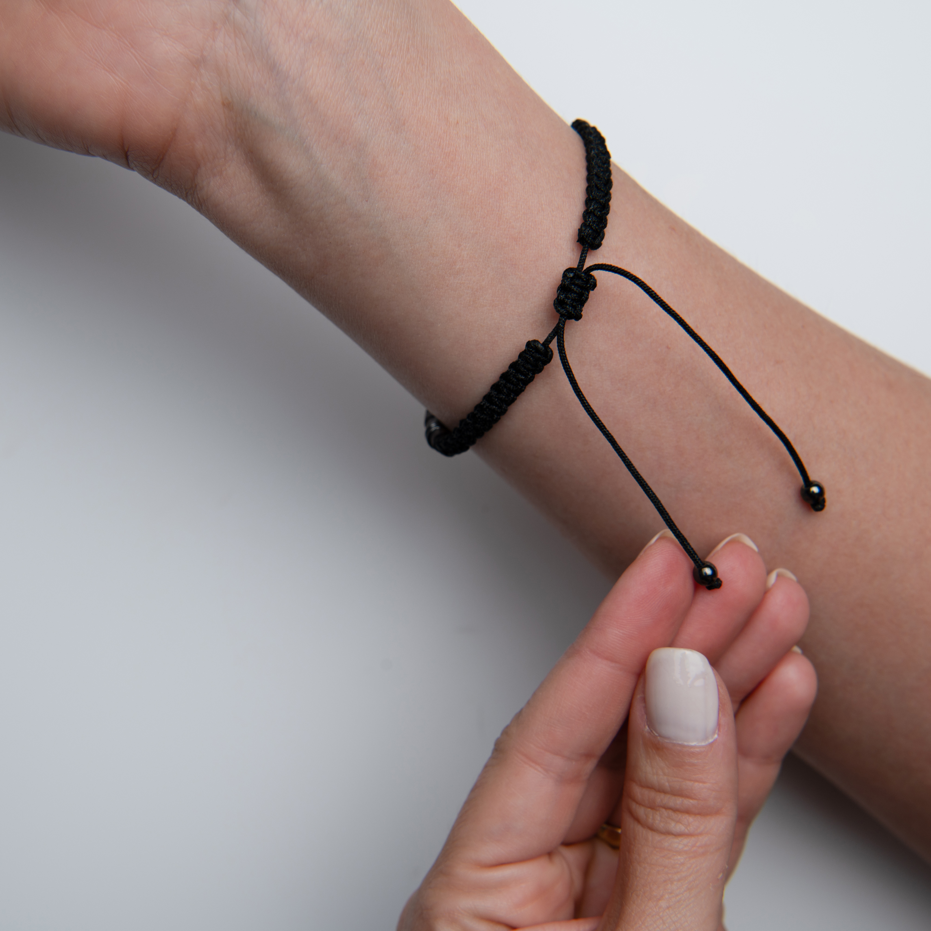 Bracelet image before retouching, showing a black cord bracelet being adjusted on the wrist