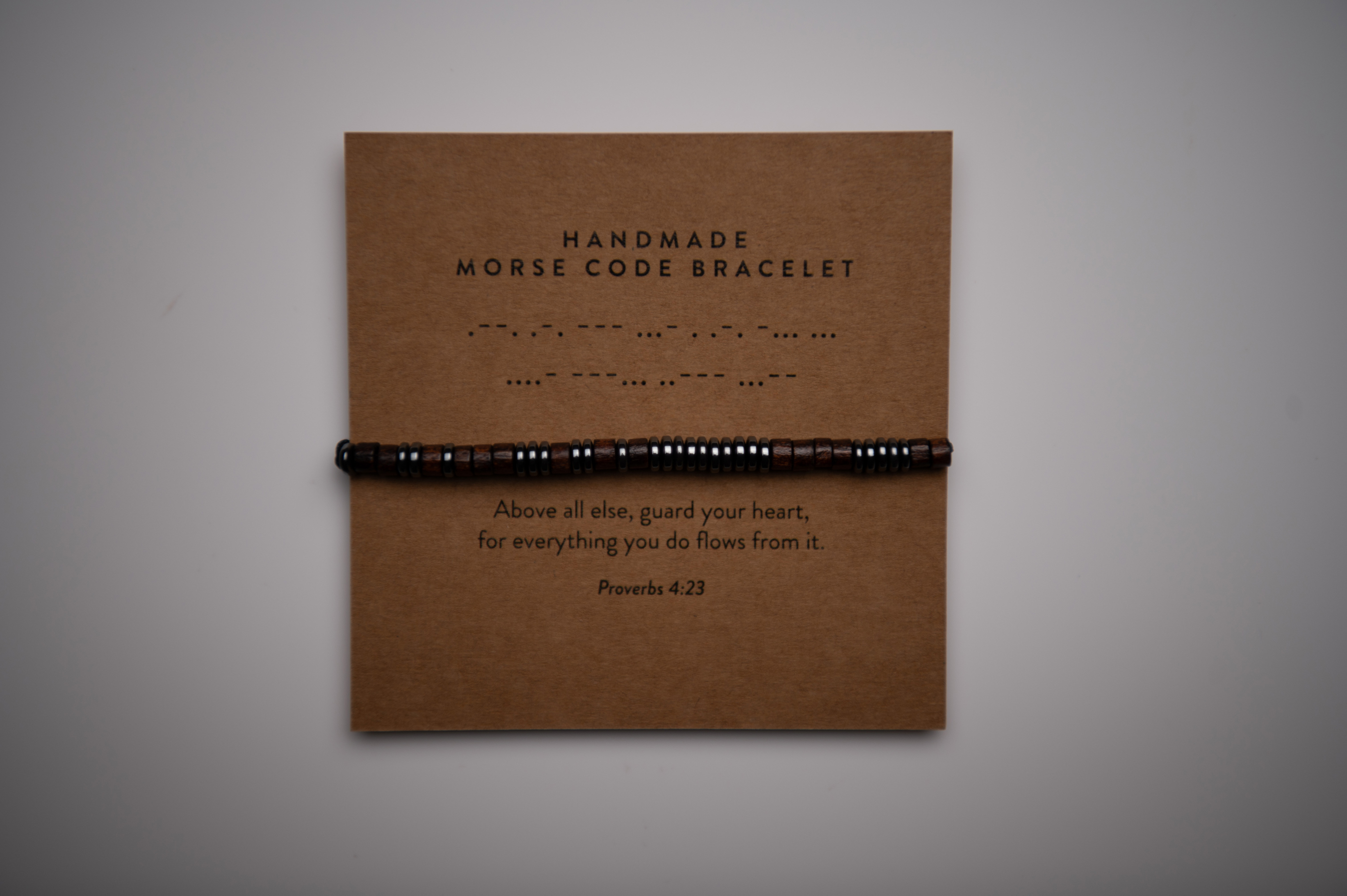 Morse code bracelet product image before retouching, photographed on a kraft display card against a gray background