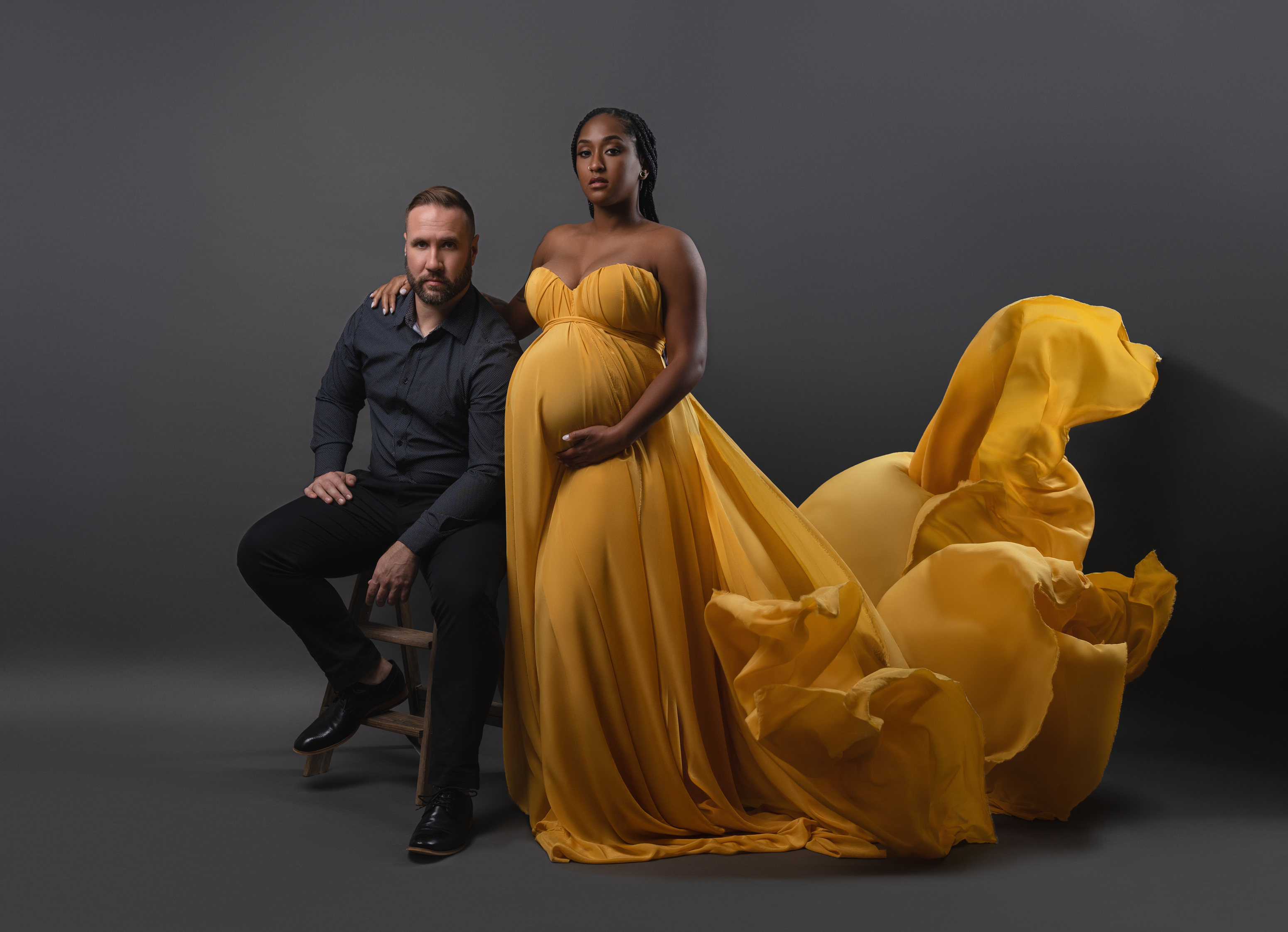 Studio maternity portrait of an expecting couple with a flowing golden gown and dramatic fabric movement