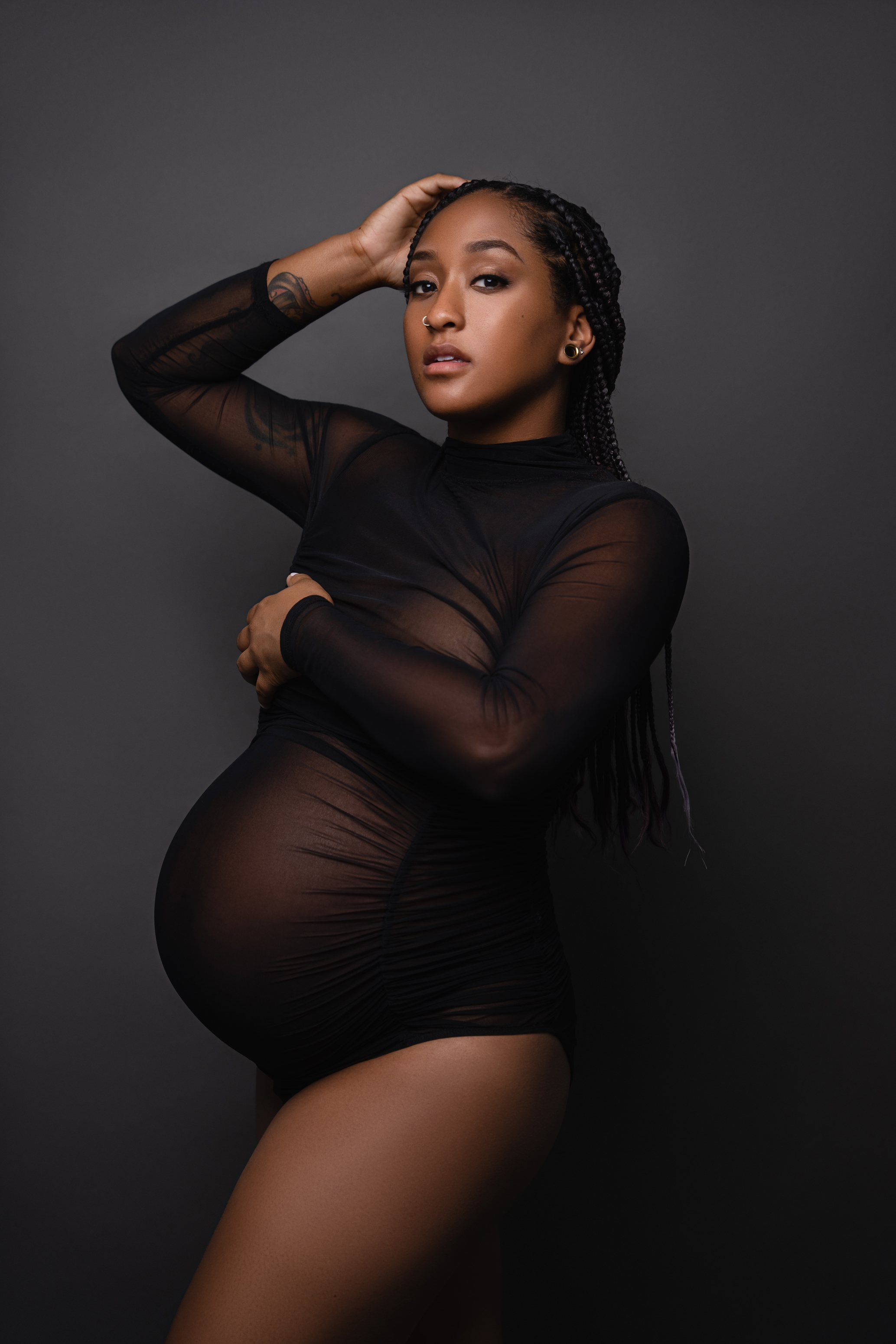 Moody maternity portrait in a sheer black outfit with soft directional studio lighting