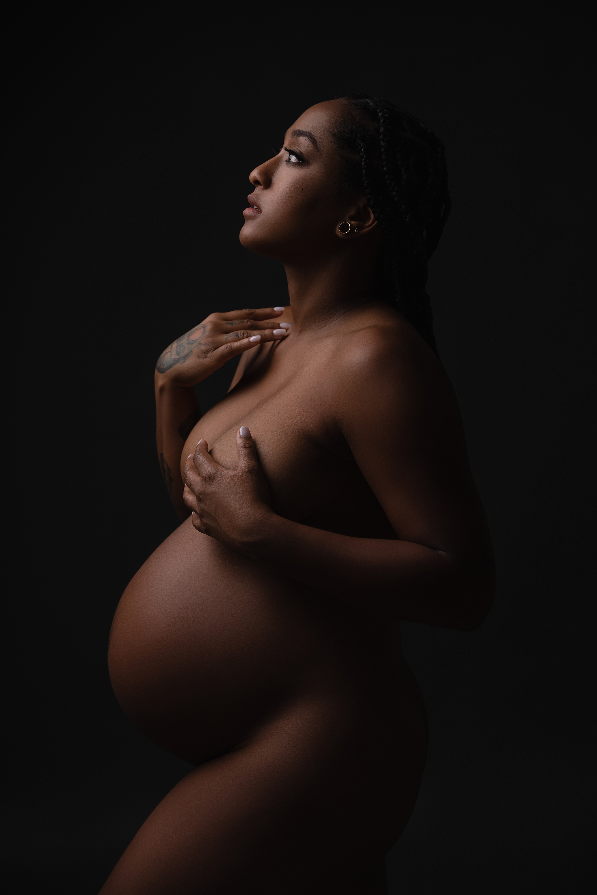 Side-profile maternity portrait with natural skin tones and soft low-key lighting against a dark background