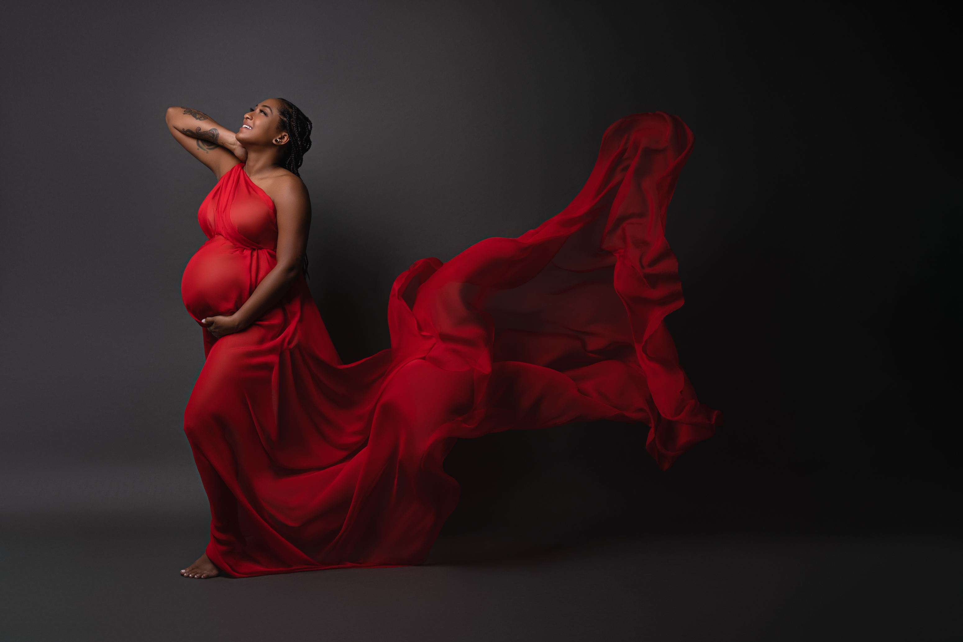 Dynamic maternity portrait in a vivid red gown with flowing fabric against a dark studio background