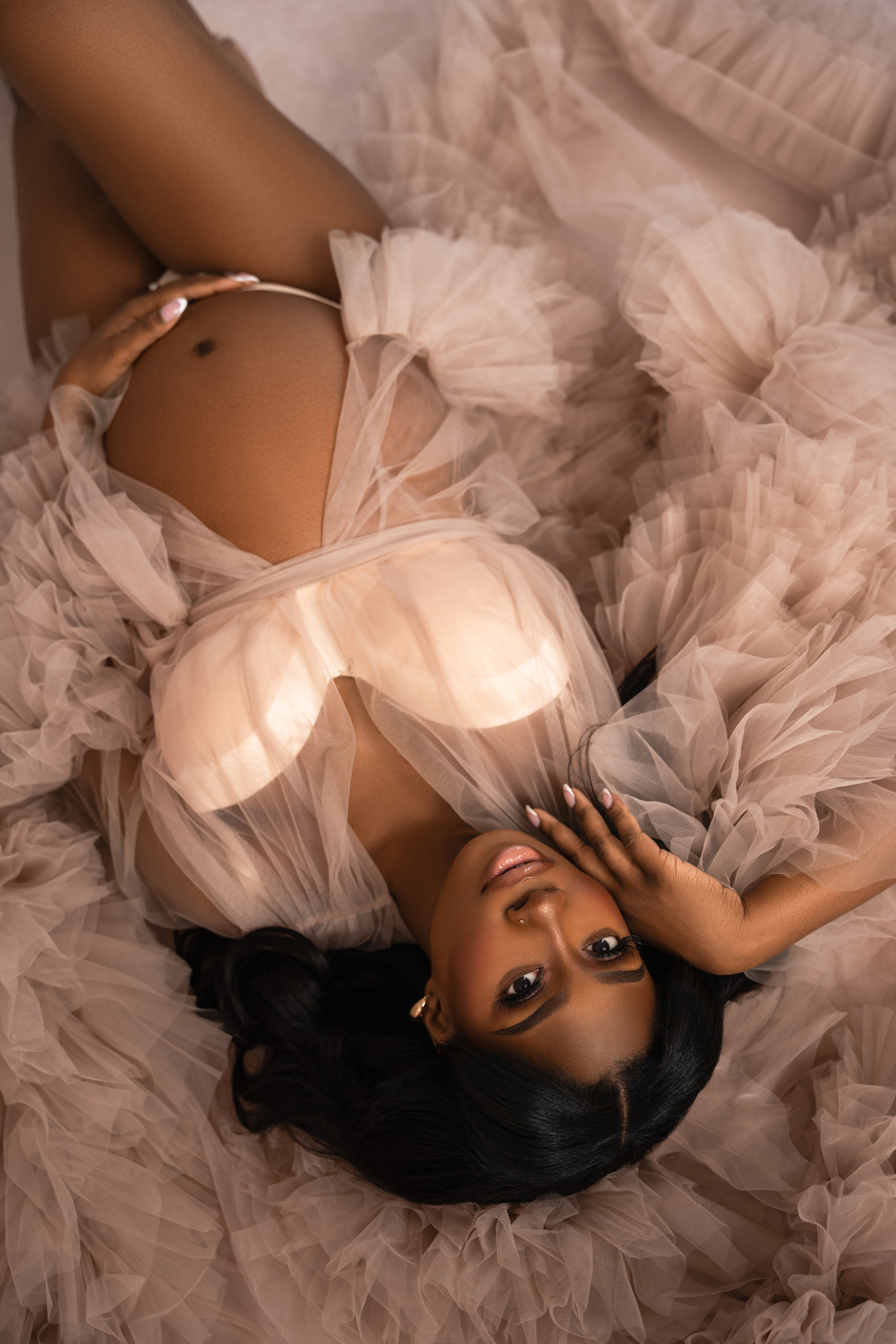 Top-down maternity portrait surrounded by layers of soft blush tulle and warm neutral fabric