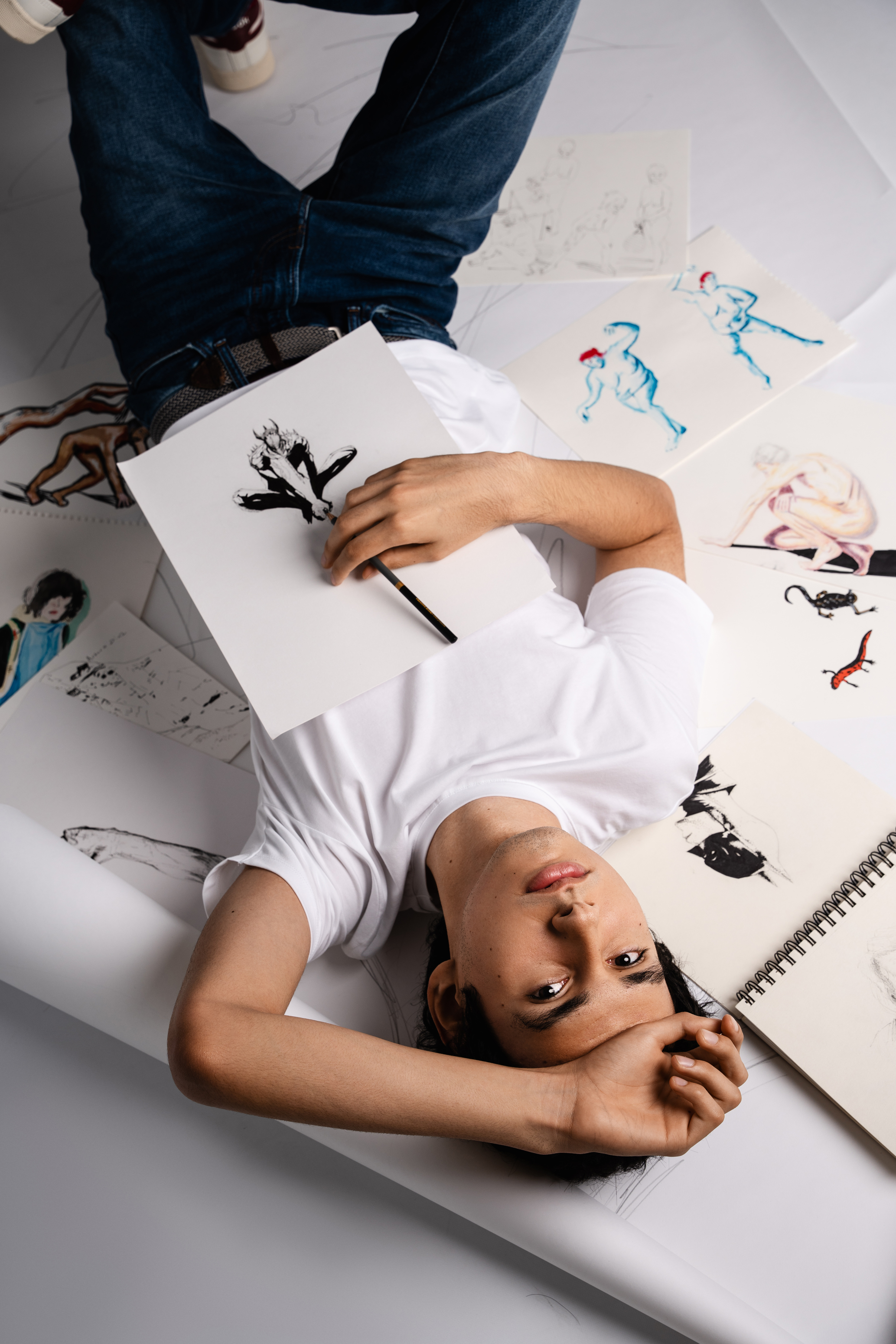 Creative personal branding portrait of a man reclining among sketchbooks and drawings in a bright studio