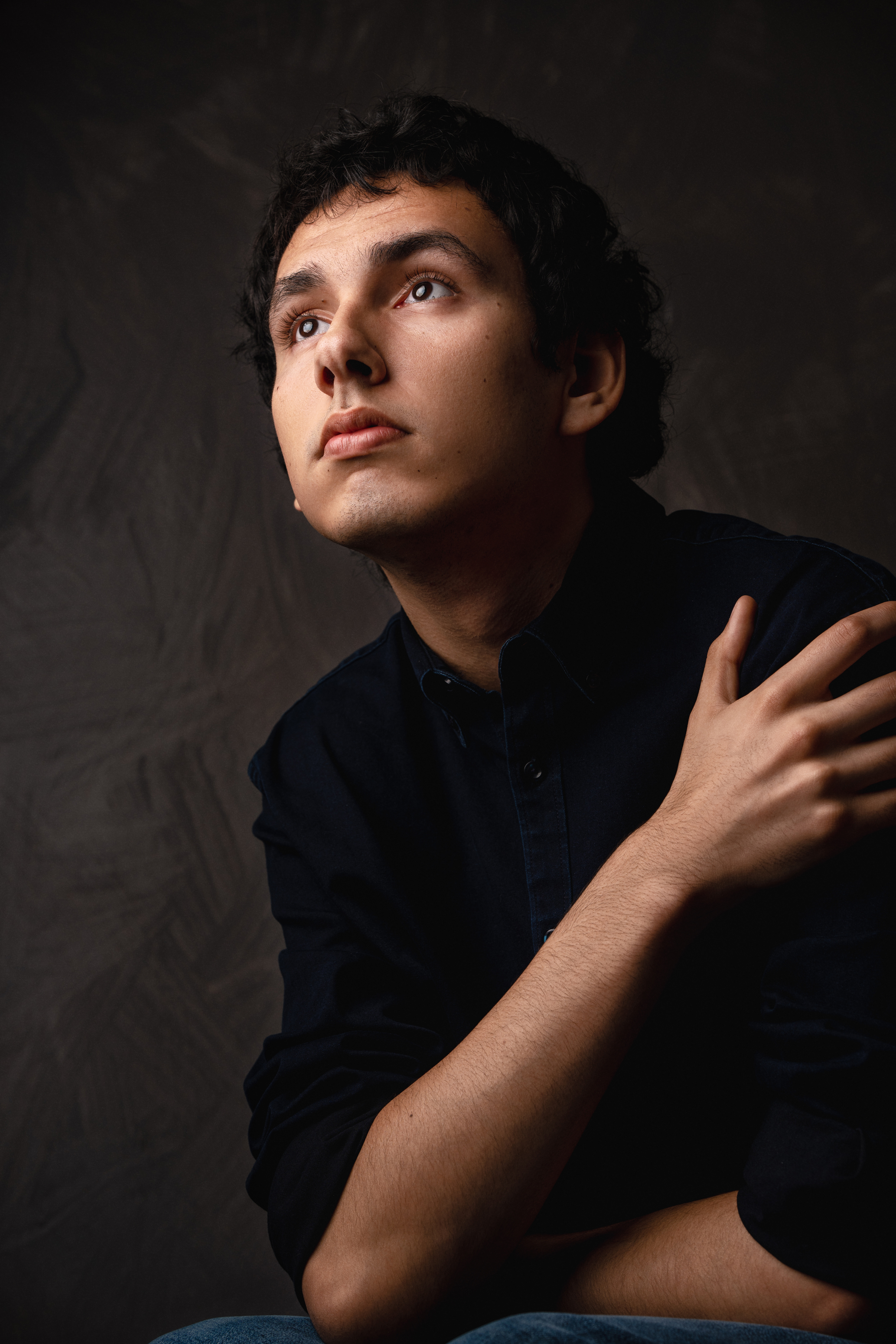 Moody studio portrait of a man in a dark shirt looking upward against a textured brown background