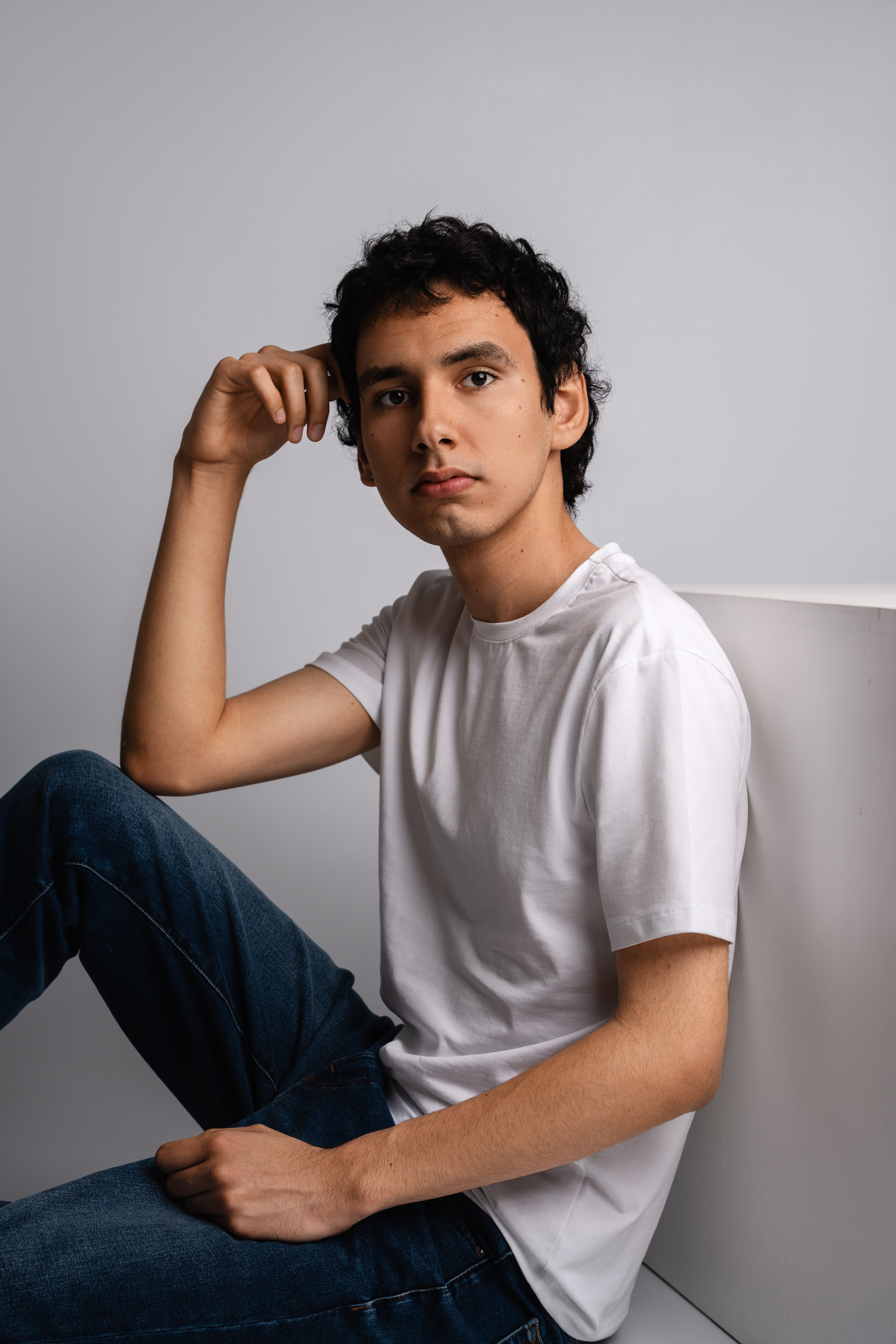 Casual personal branding portrait of a man in a white T-shirt and jeans seated in a minimal studio