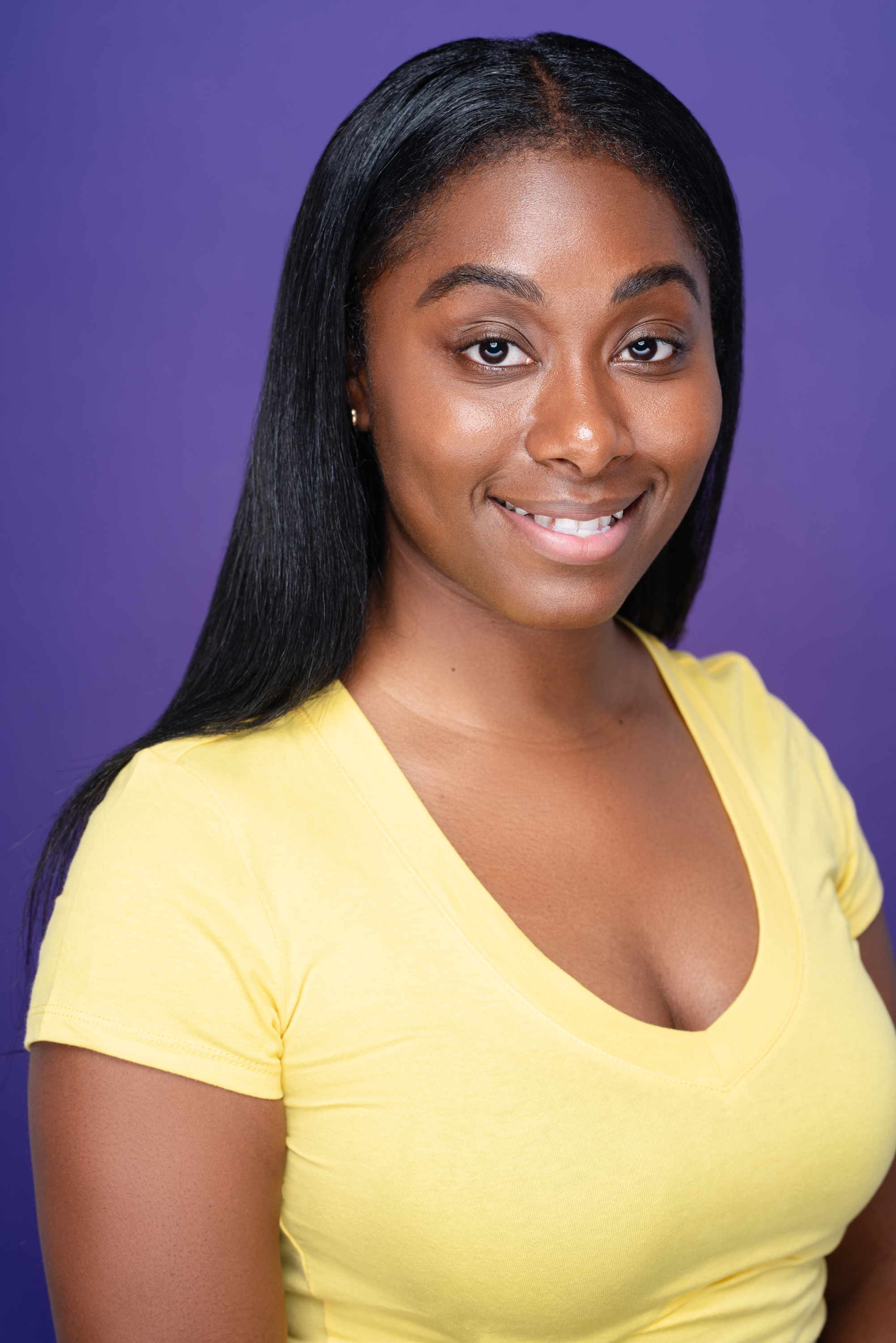 Studio portrait of a woman in a yellow top against a vivid violet background