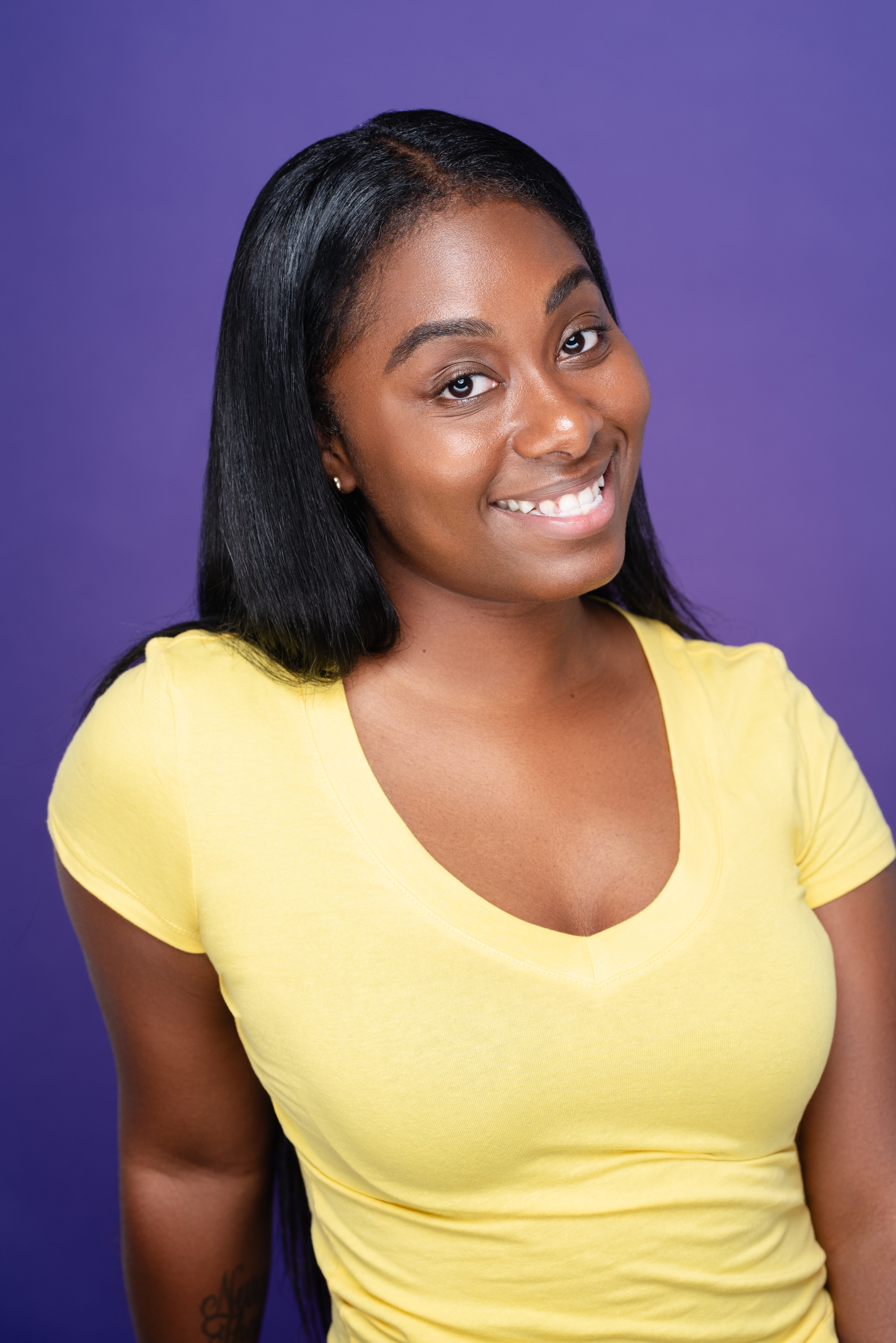 Smiling studio portrait of a woman in a yellow top against a rich violet background