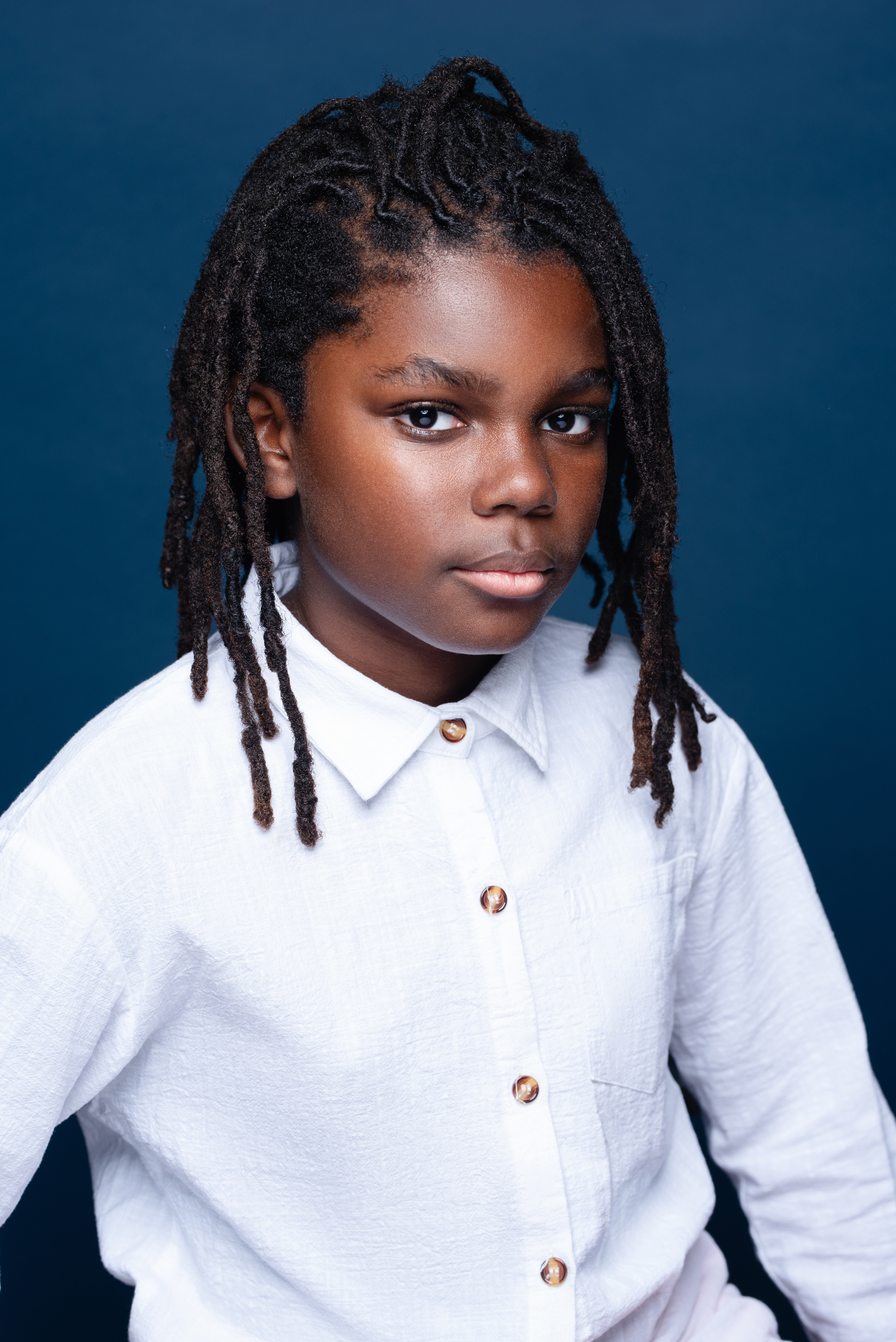 Studio portrait of a child with locs in a white shirt against a rich blue background