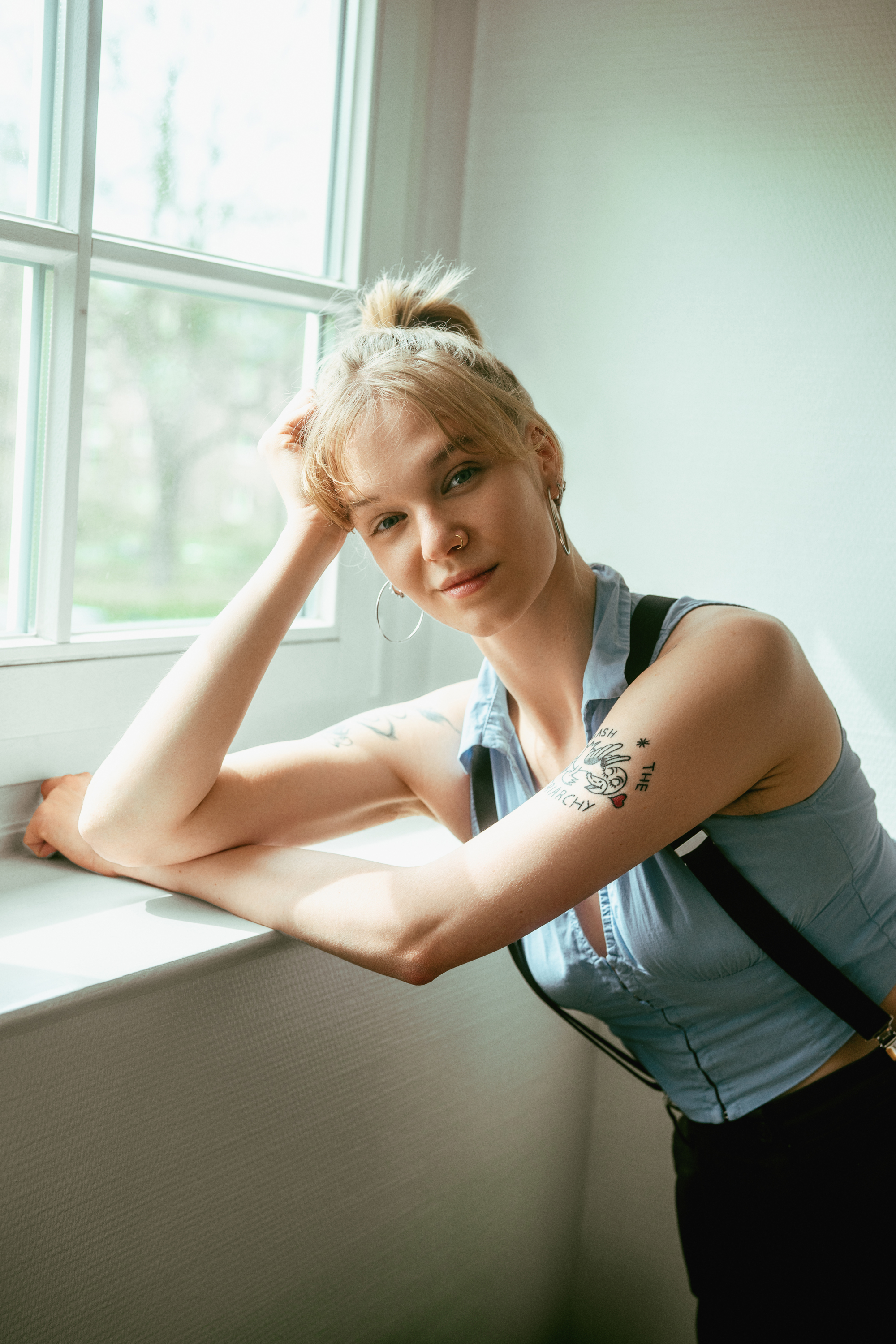 Soft natural-light portrait of a woman leaning beside a window in a pale blue top