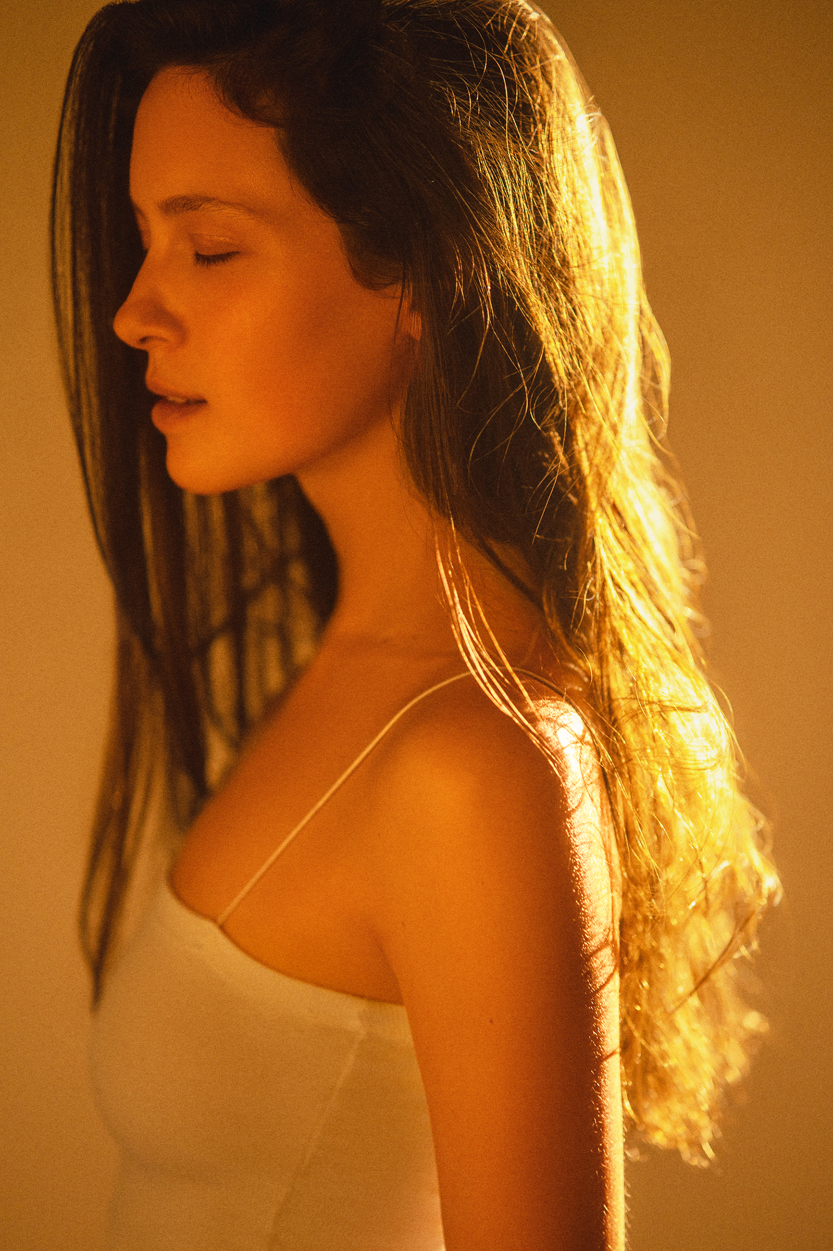 Side-profile portrait of a woman with long dark hair illuminated by warm golden backlight