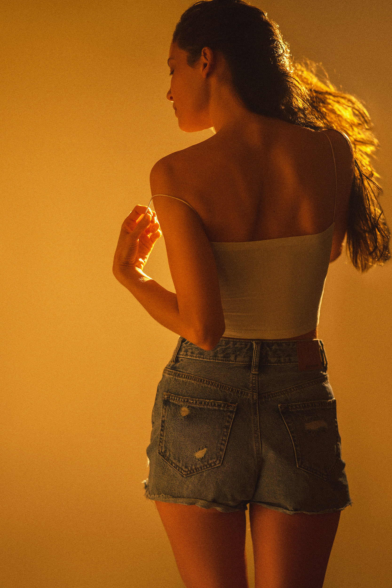 Back-view portrait of a woman in denim shorts with her hair illuminated by strong golden rim light