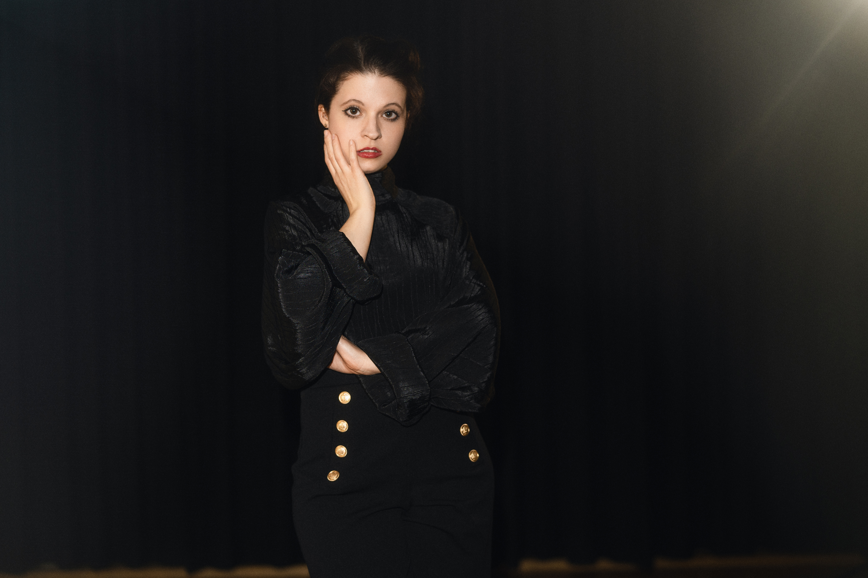 Moody editorial portrait of a woman dressed in black against a dark studio backdrop with soft directional light