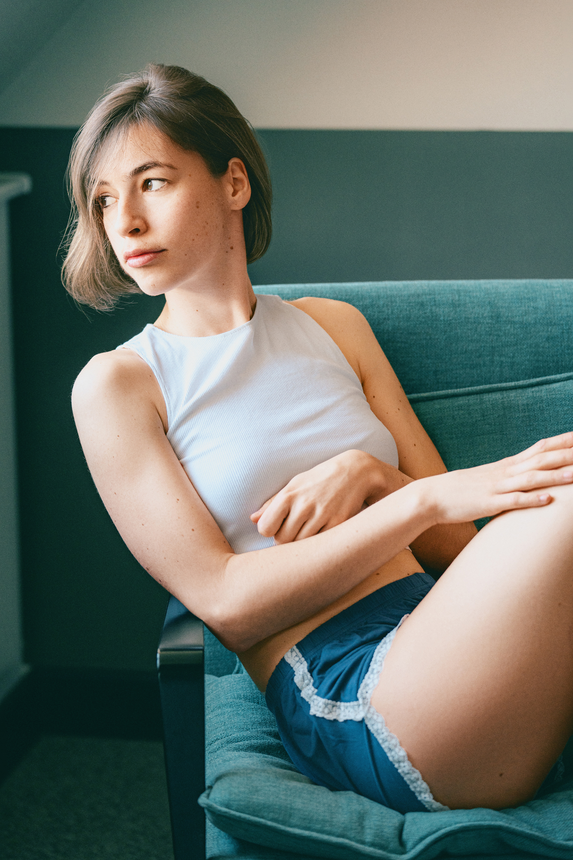 Relaxed portrait of a short-haired woman reclining in a teal armchair with soft warm skin tones