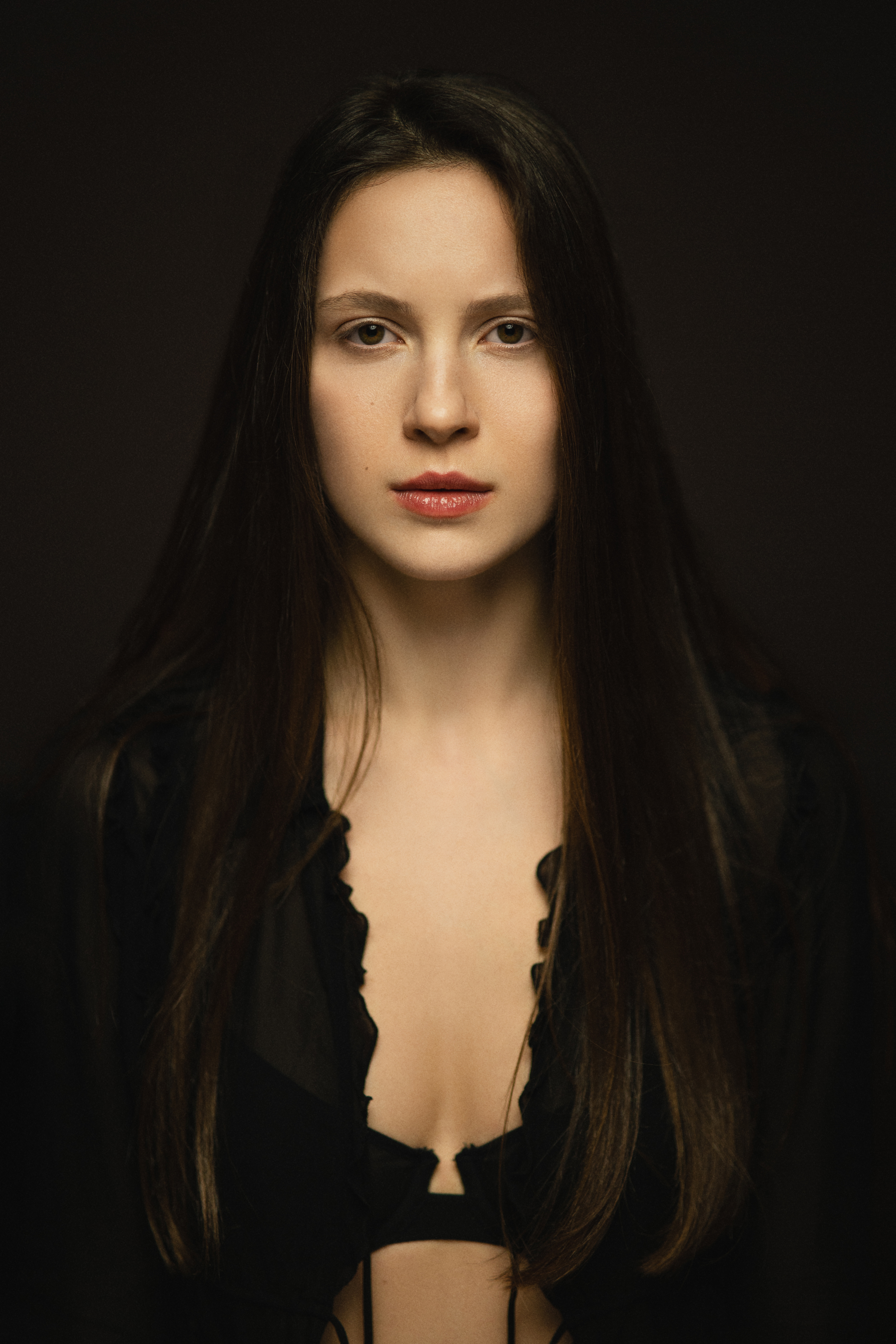 Moody close-up portrait of a woman with long dark hair in black styling against a deep shadowed background