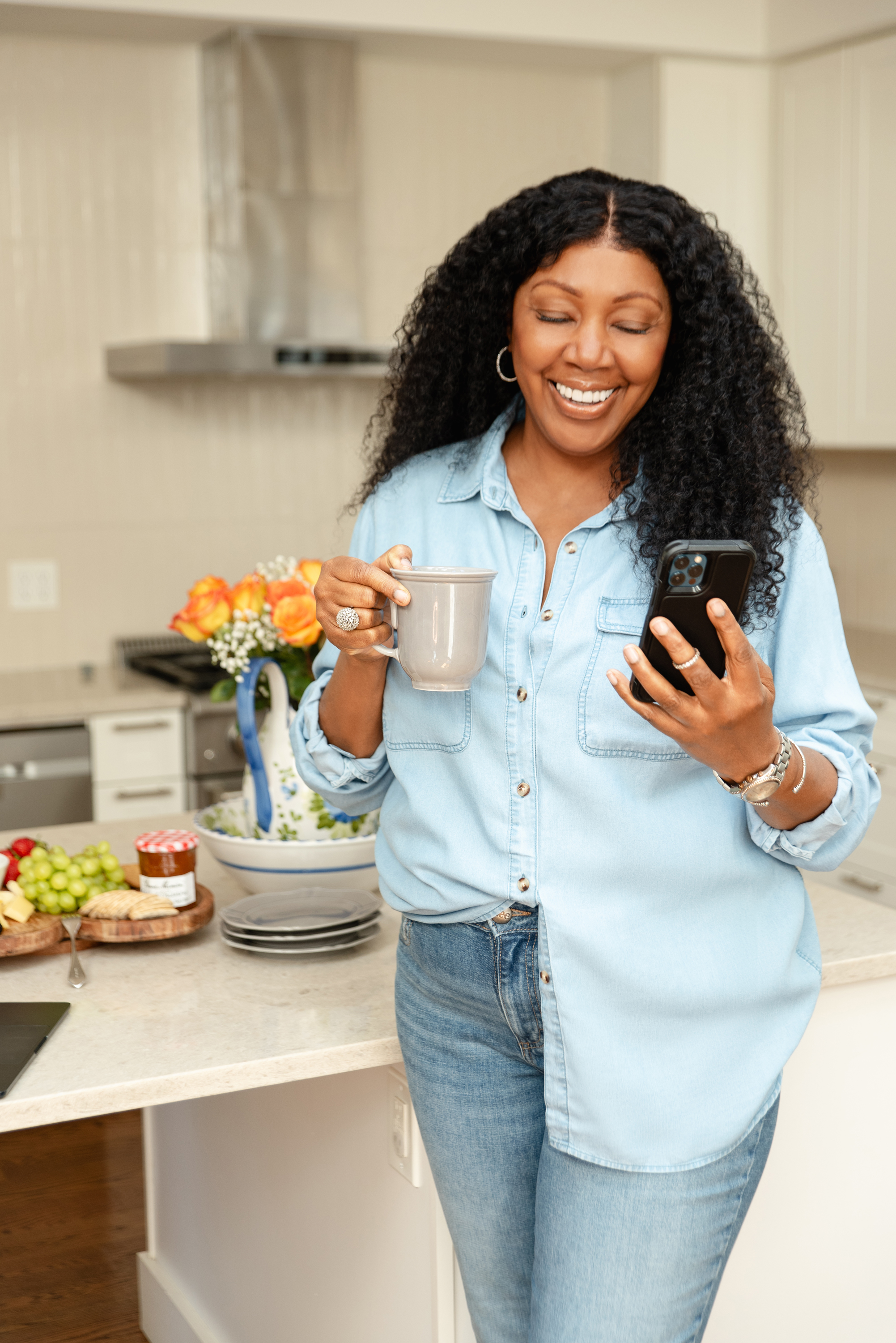 Lifestyle personal branding portrait of a woman holding a coffee mug and smartphone in a bright modern kitchen