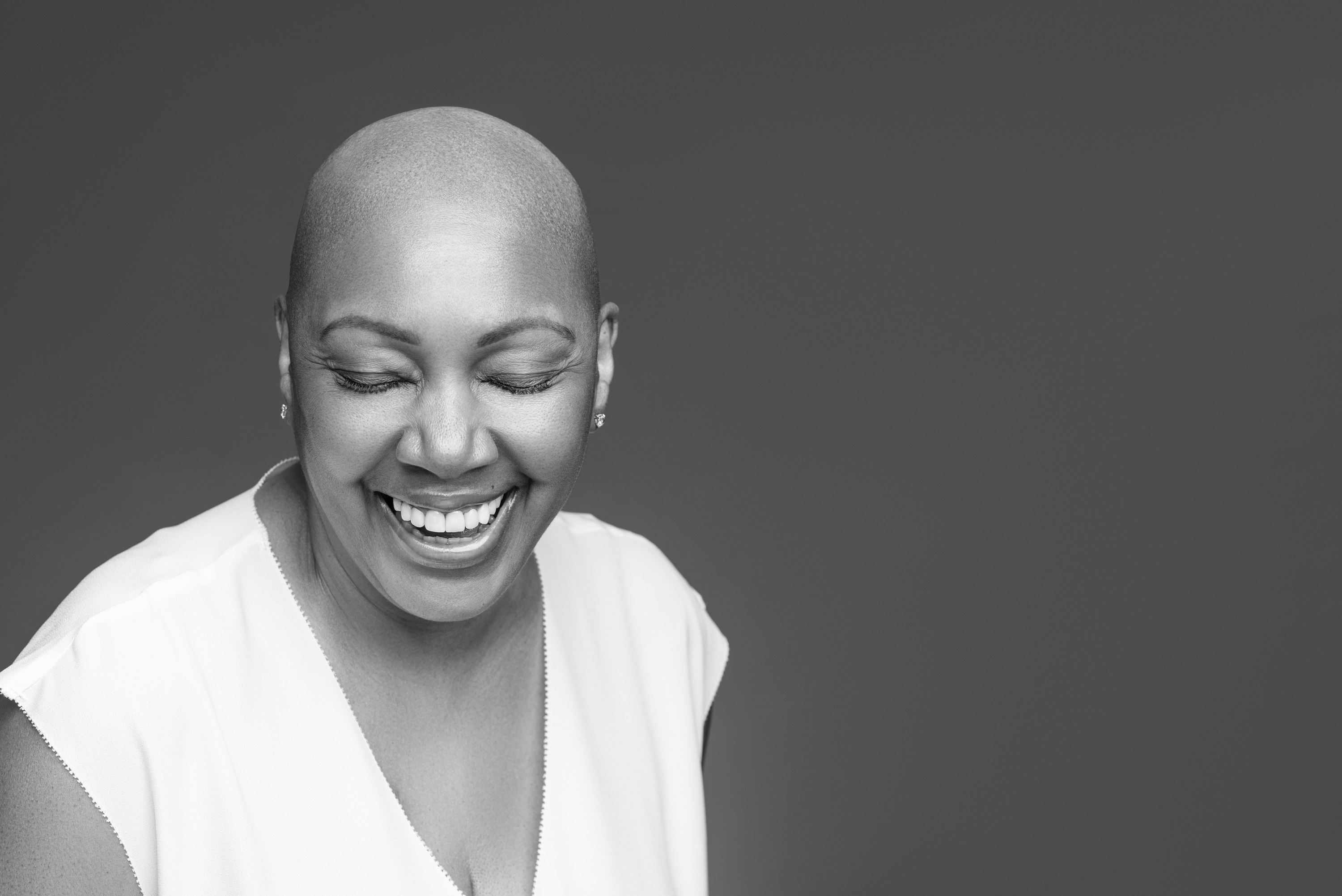 Expressive black-and-white portrait of a smiling woman with a shaved head against a dark studio background