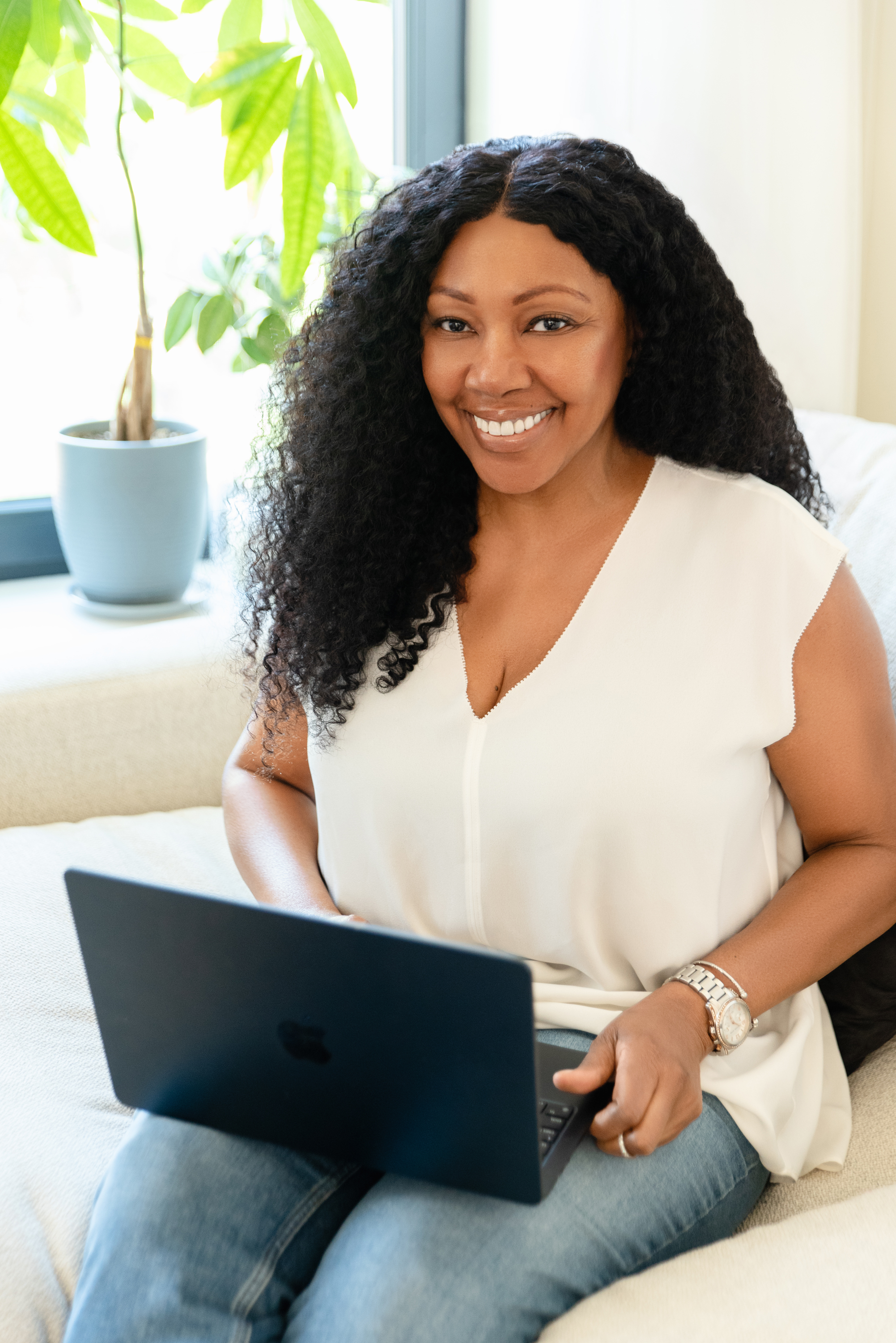 Lifestyle portrait of a woman with long curly hair seated with a laptop in a bright home interior