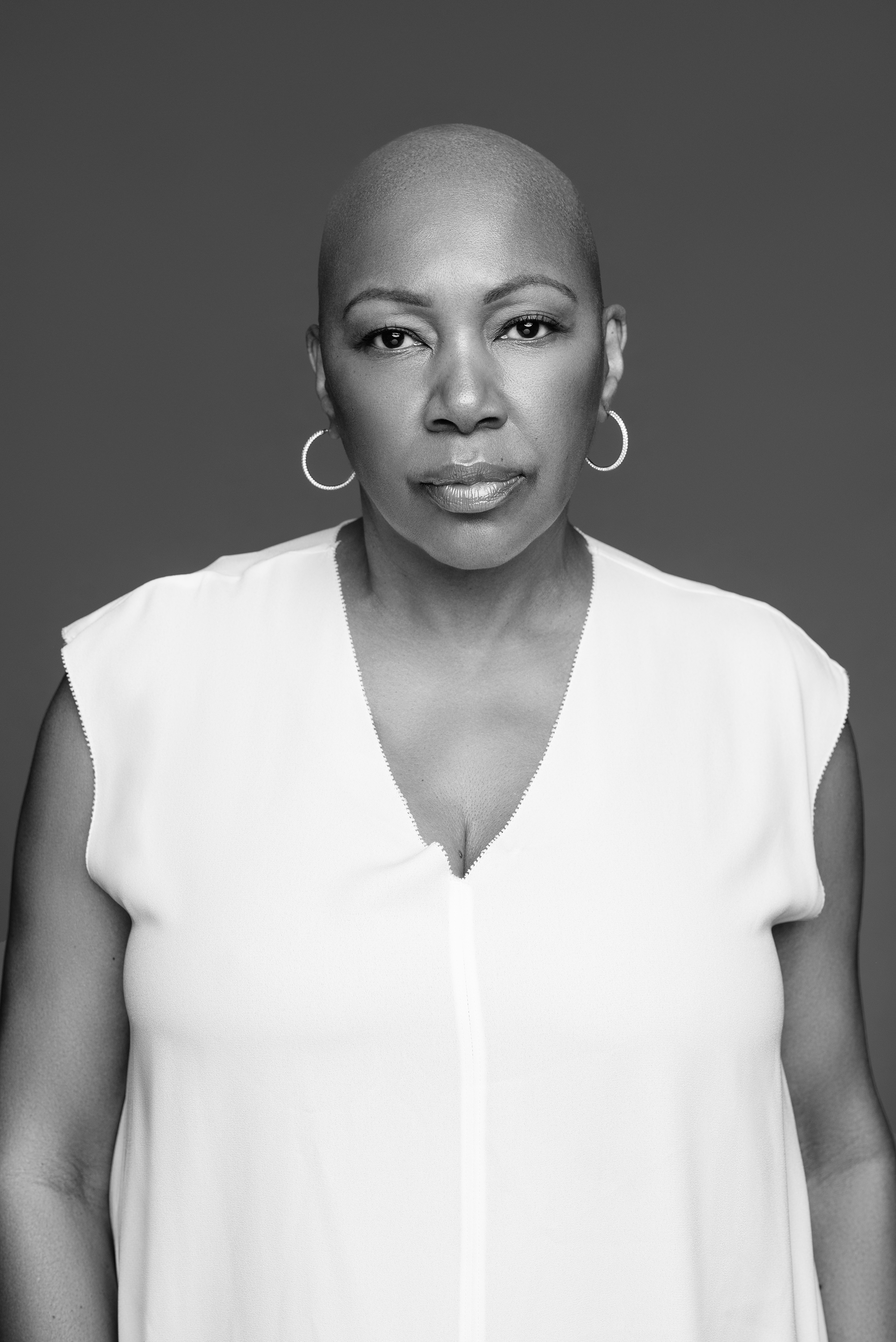 Black-and-white studio portrait of a woman with a shaved head wearing a white sleeveless top
