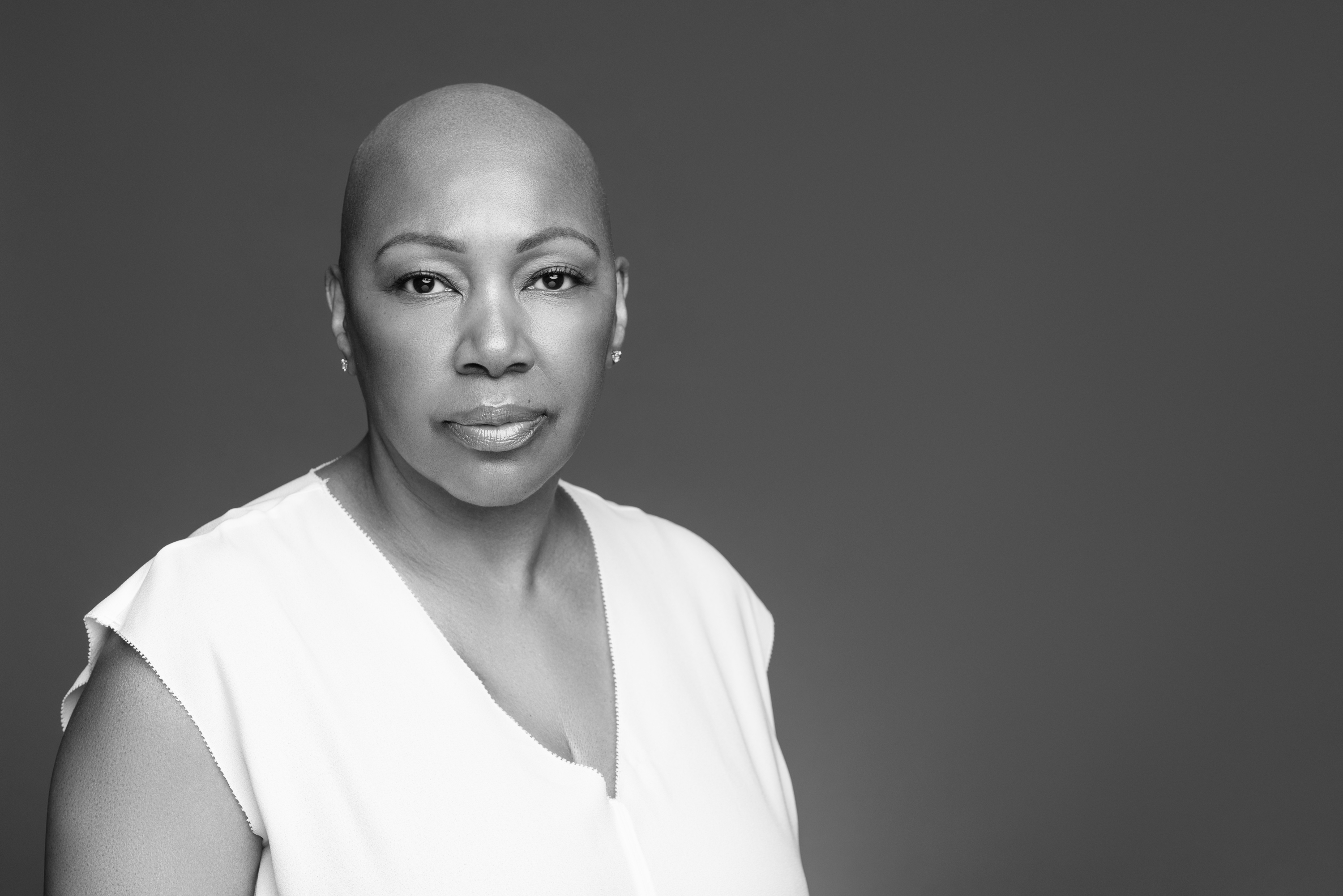 Black-and-white studio portrait of a woman with a shaved head and a calm direct expression