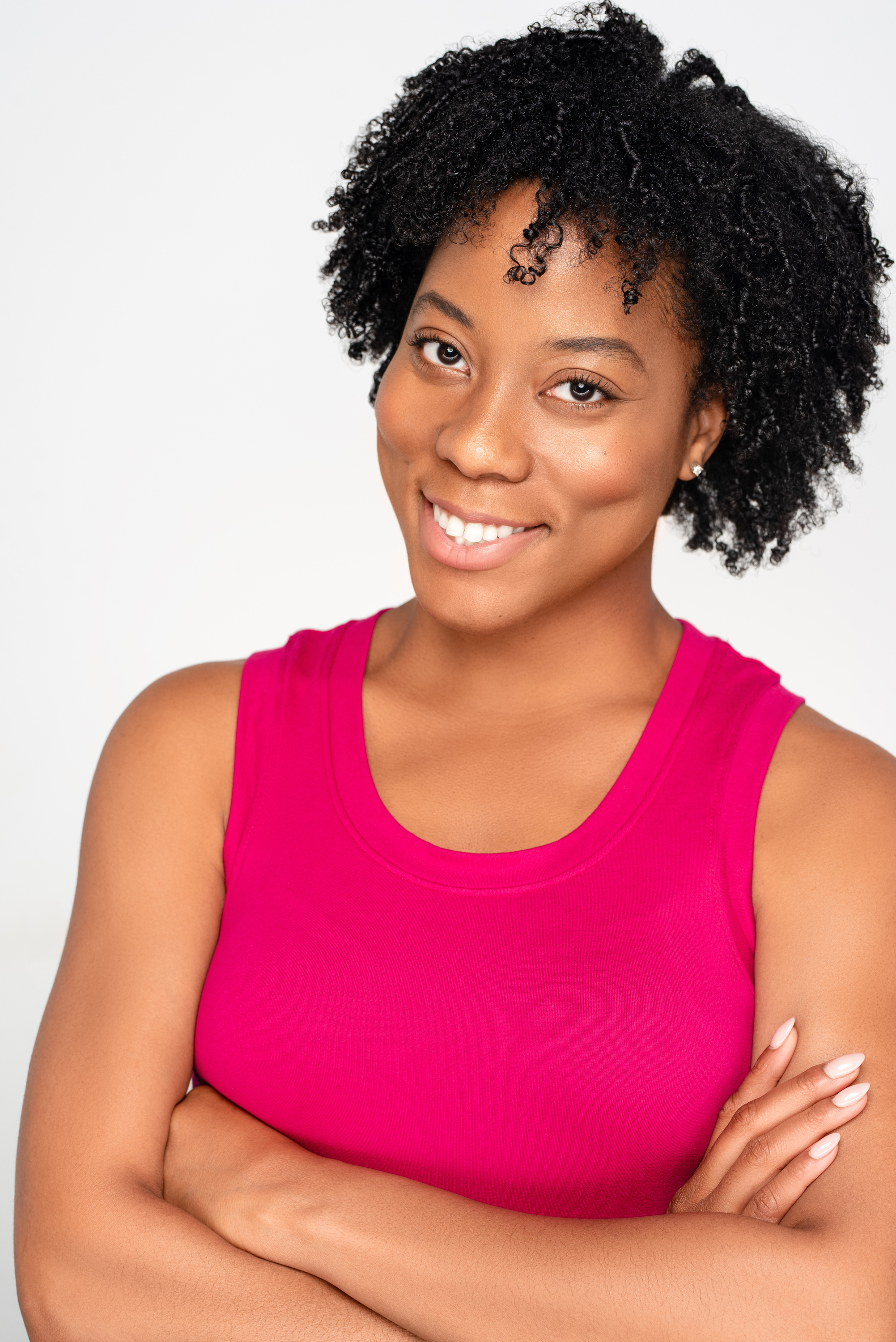 Smiling studio headshot of a woman with natural curly hair in a bright pink top against a light background
