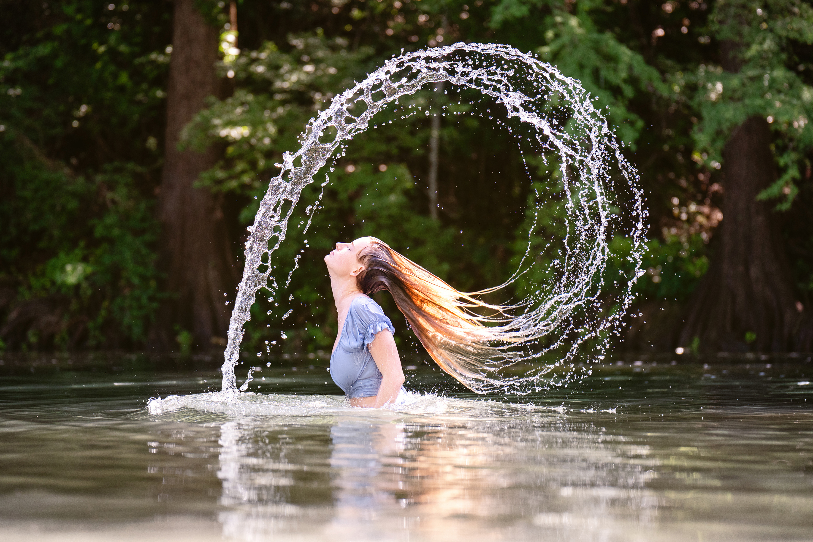 Creative outdoor portrait of a young woman in water with her hair creating a circular splash