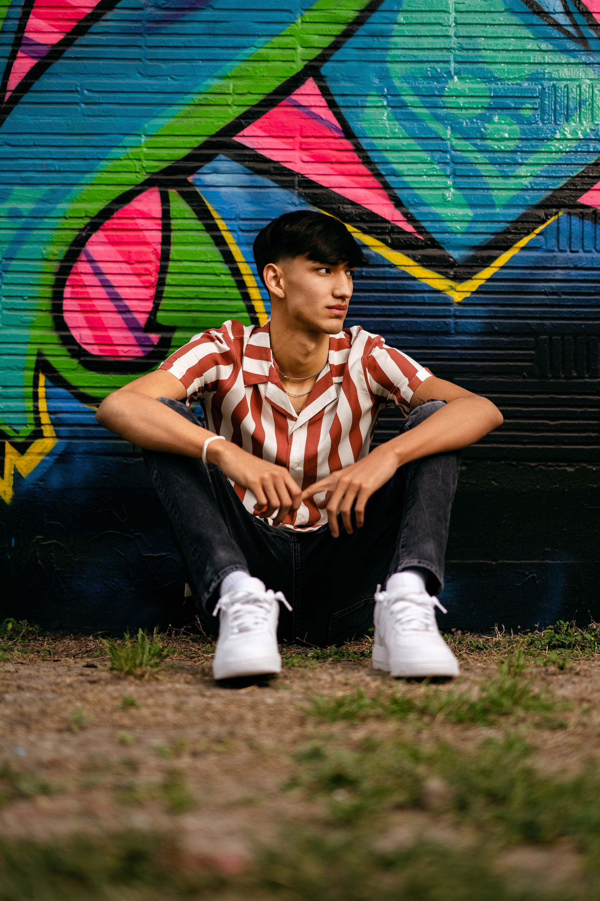senior portrait of a teenage boy sitting in front of a colorful graffiti wall