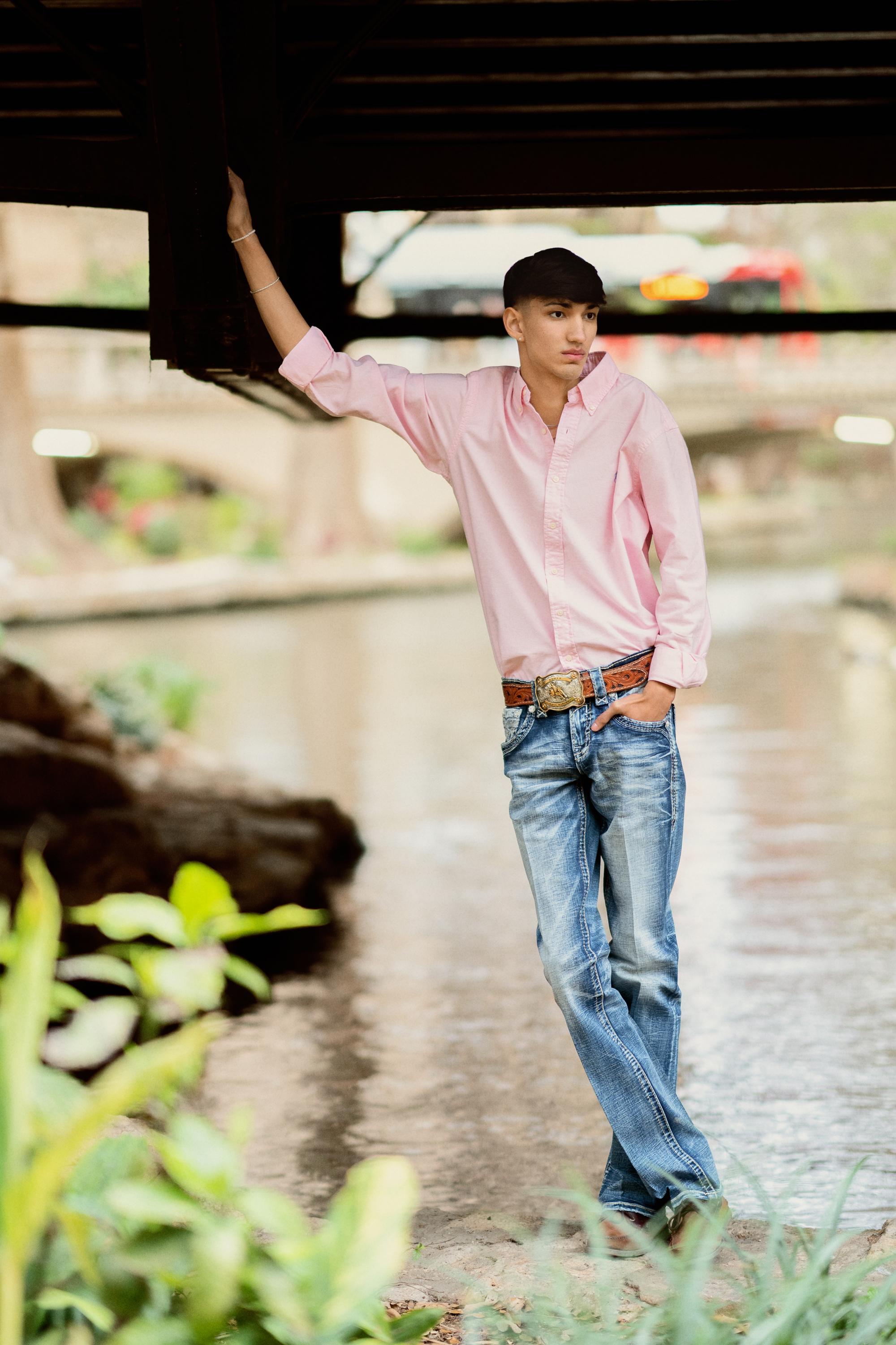 senior portrait of a teenage boy standing under a bridge by the water