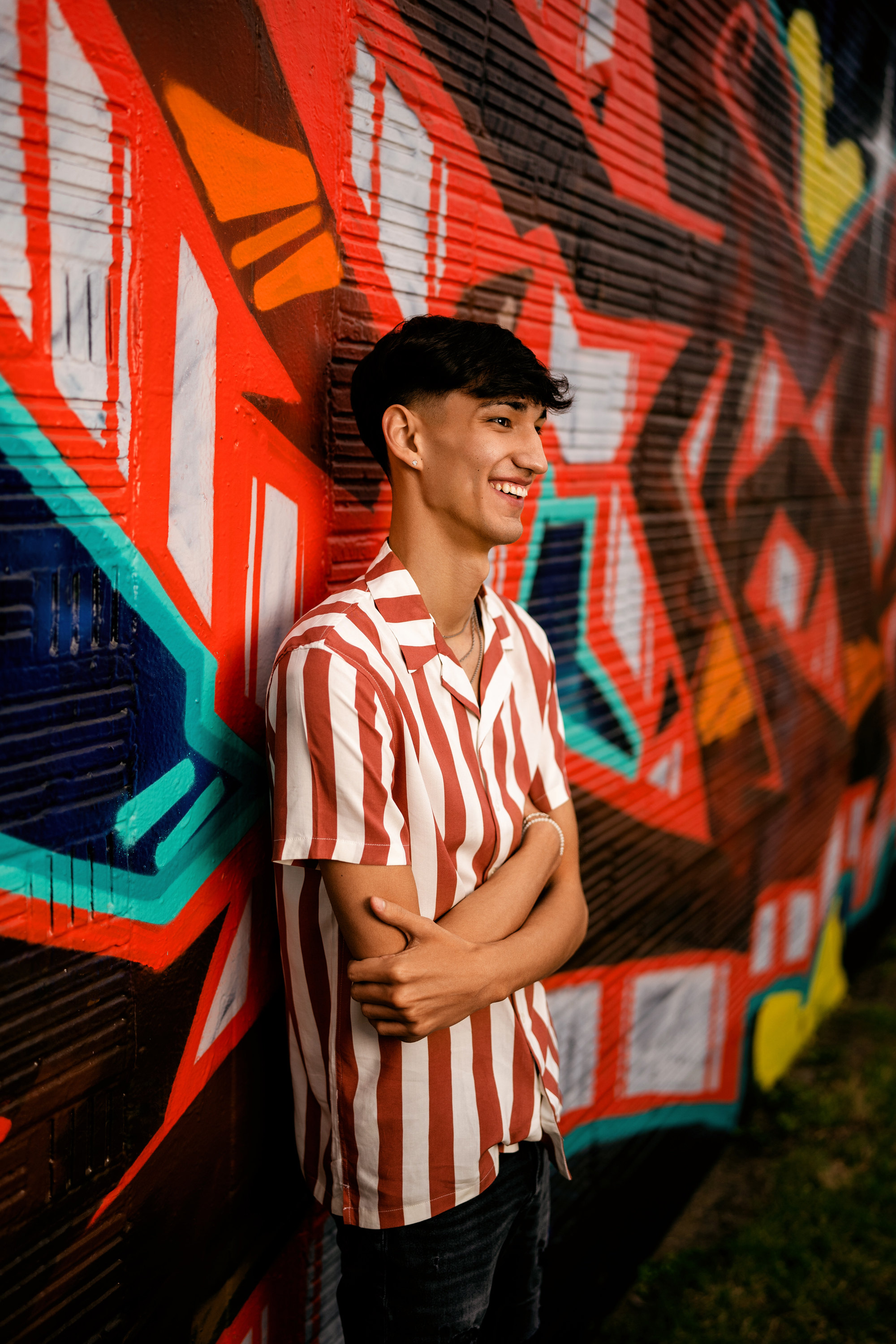 senior portrait of a smiling teenage boy standing by a graffiti wall
