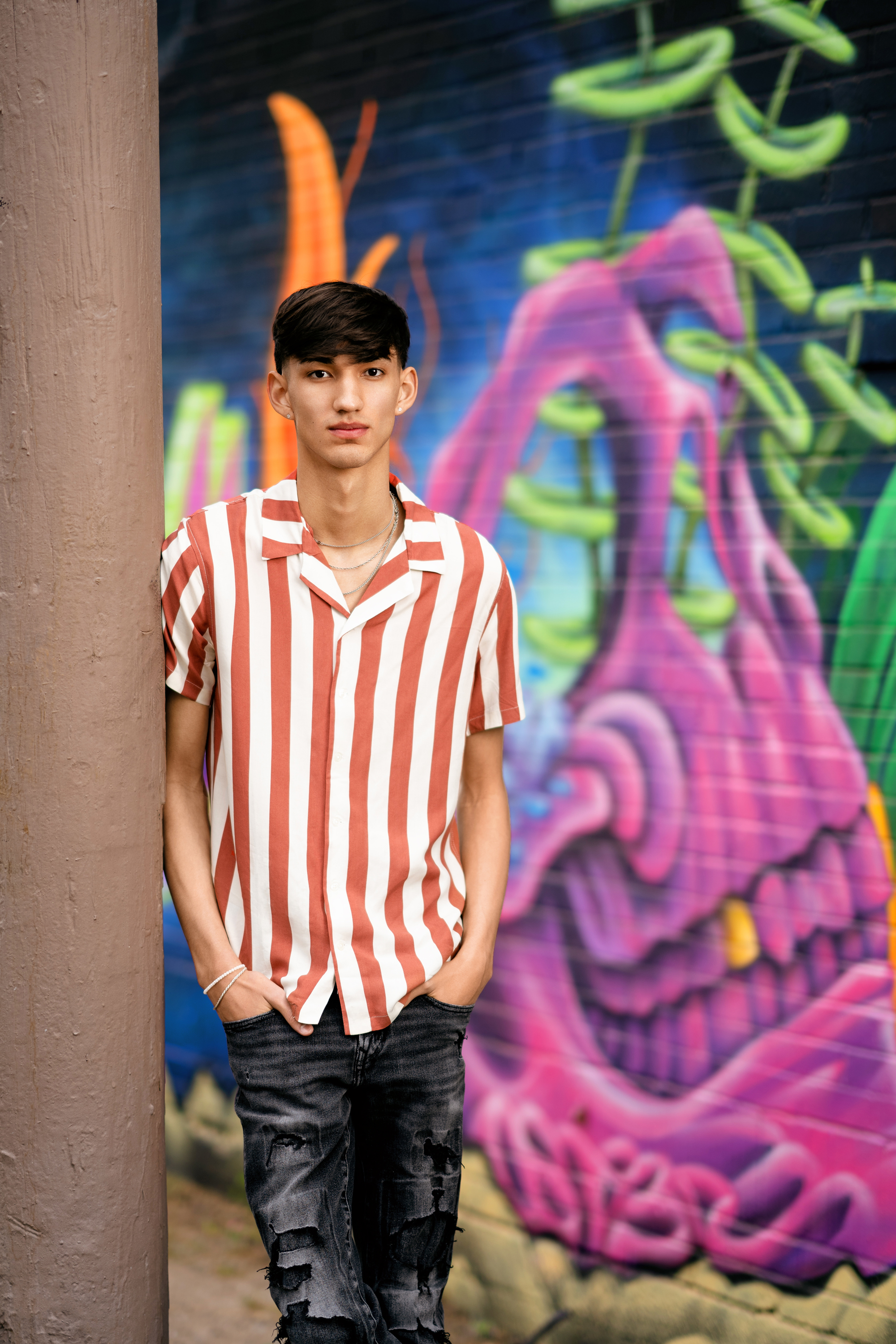 full-length senior portrait of a teenage boy standing by a colorful graffiti wall
