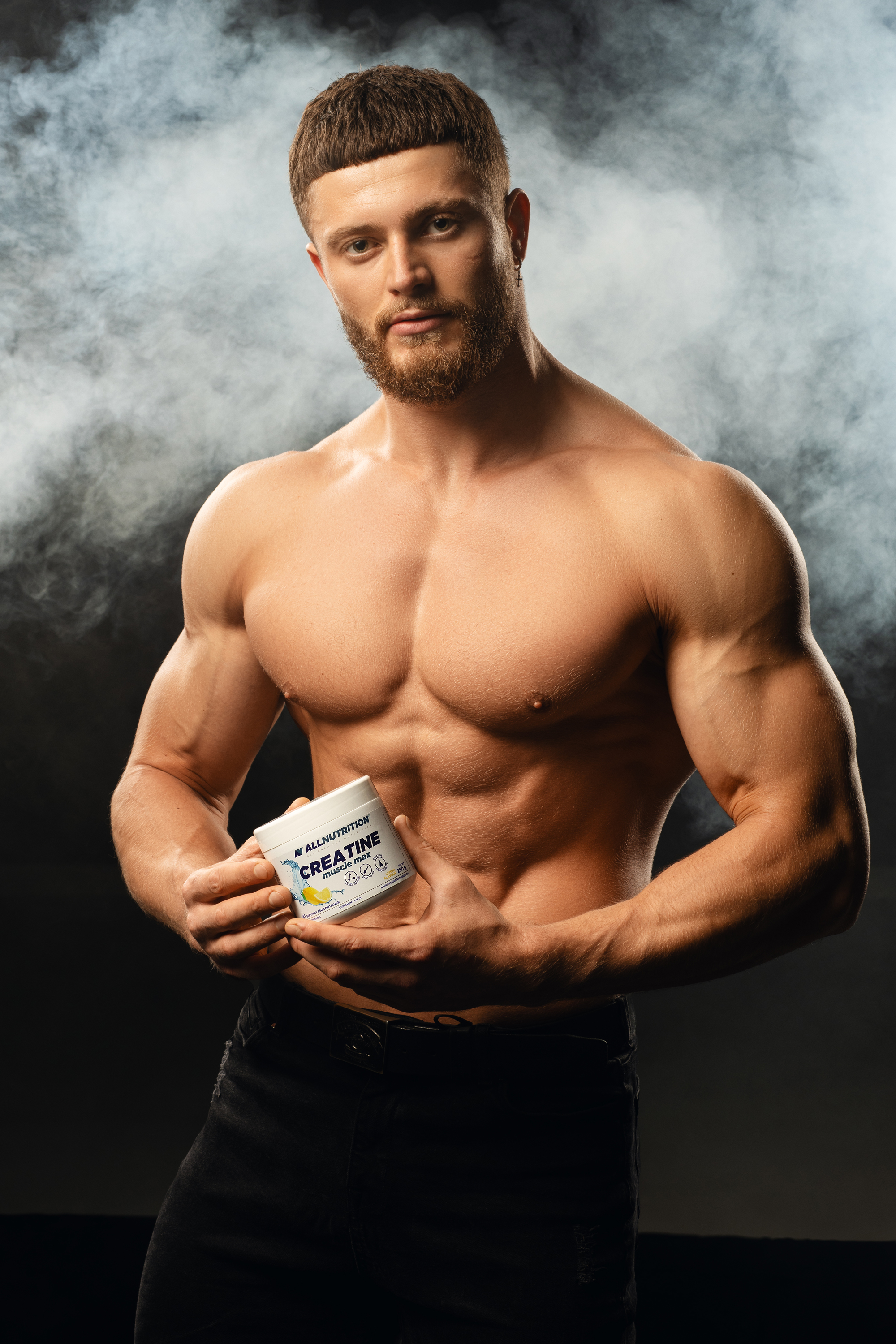Commercial sports portrait of a muscular man presenting a supplement container against a smoky dark backdrop