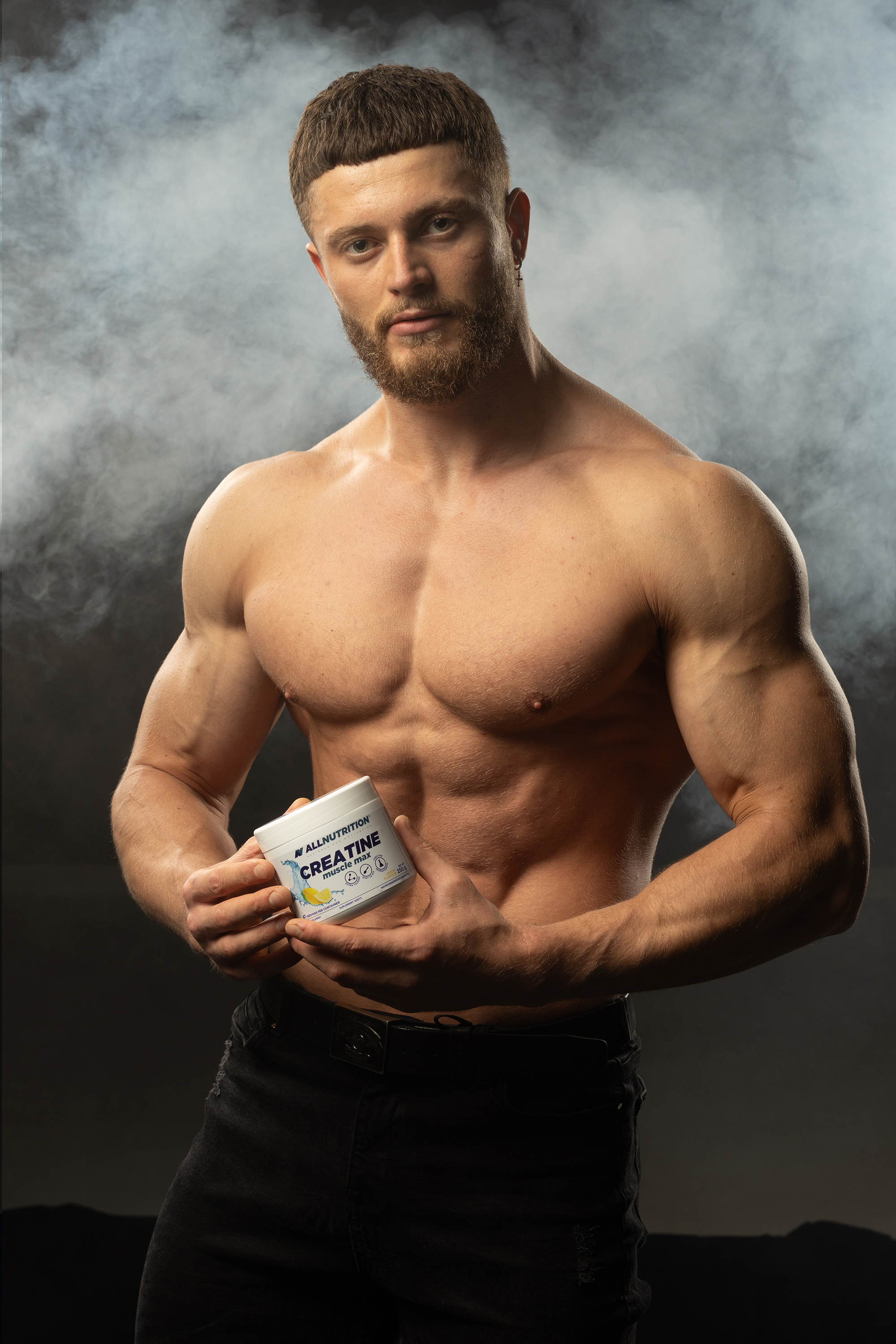 Commercial fitness image of a man holding a supplement container in hazy studio light before retouching