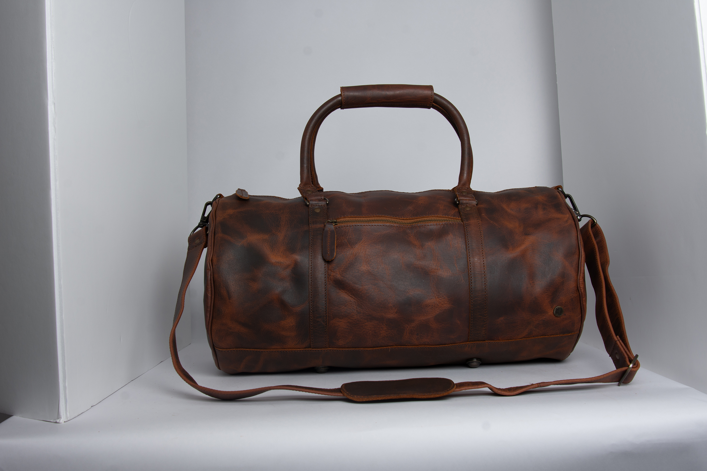Waxy brown leather duffle bag photographed inside a studio lightbox before retouching