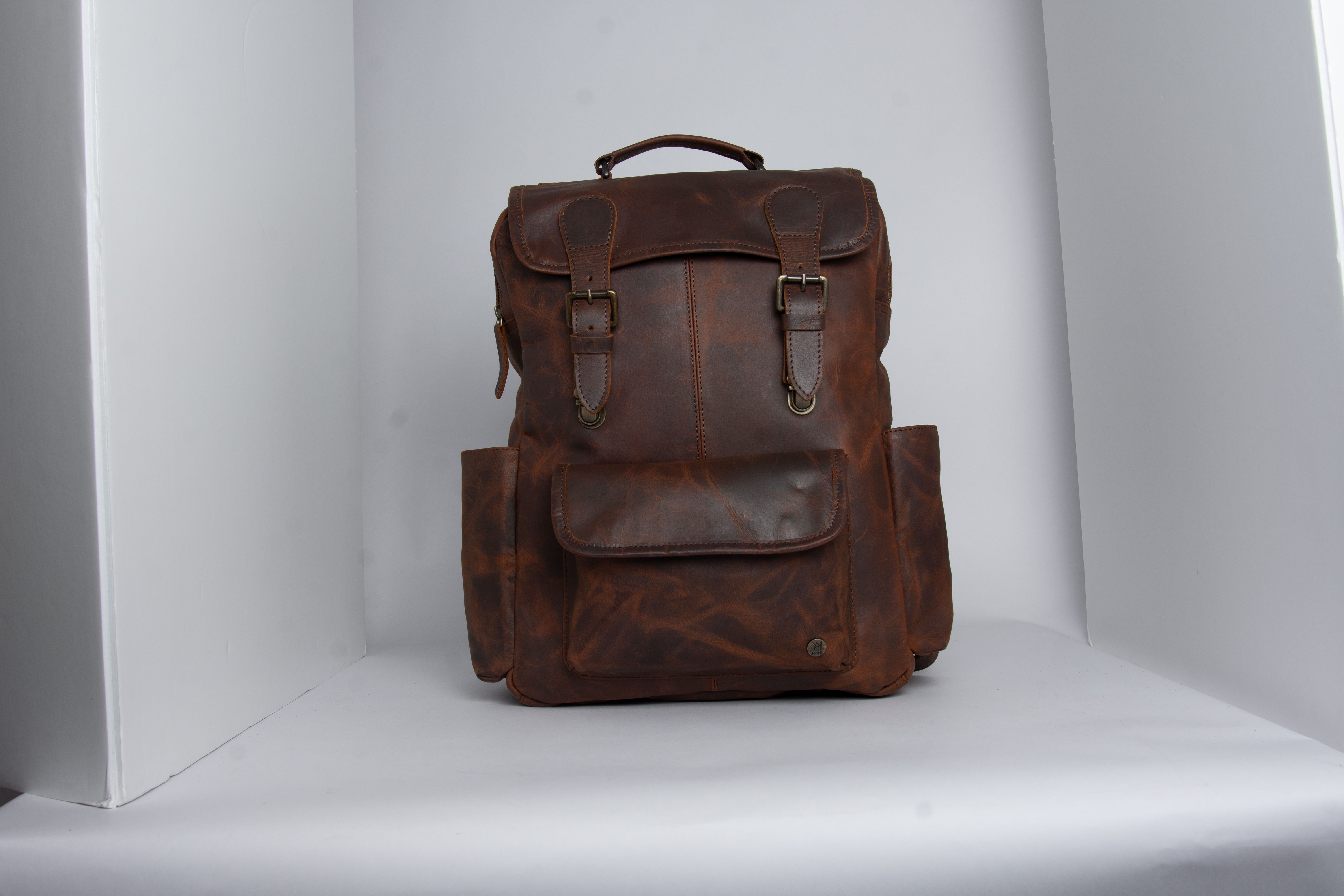 Front view of a brown leather backpack photographed in a lightbox before retouching