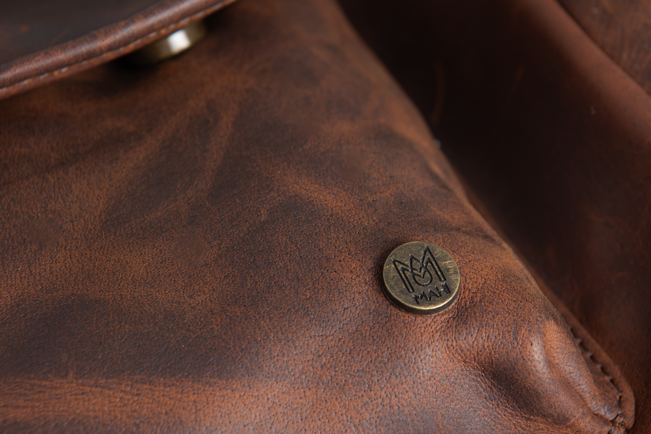Close-up of a metal logo badge on brown leather before retouching