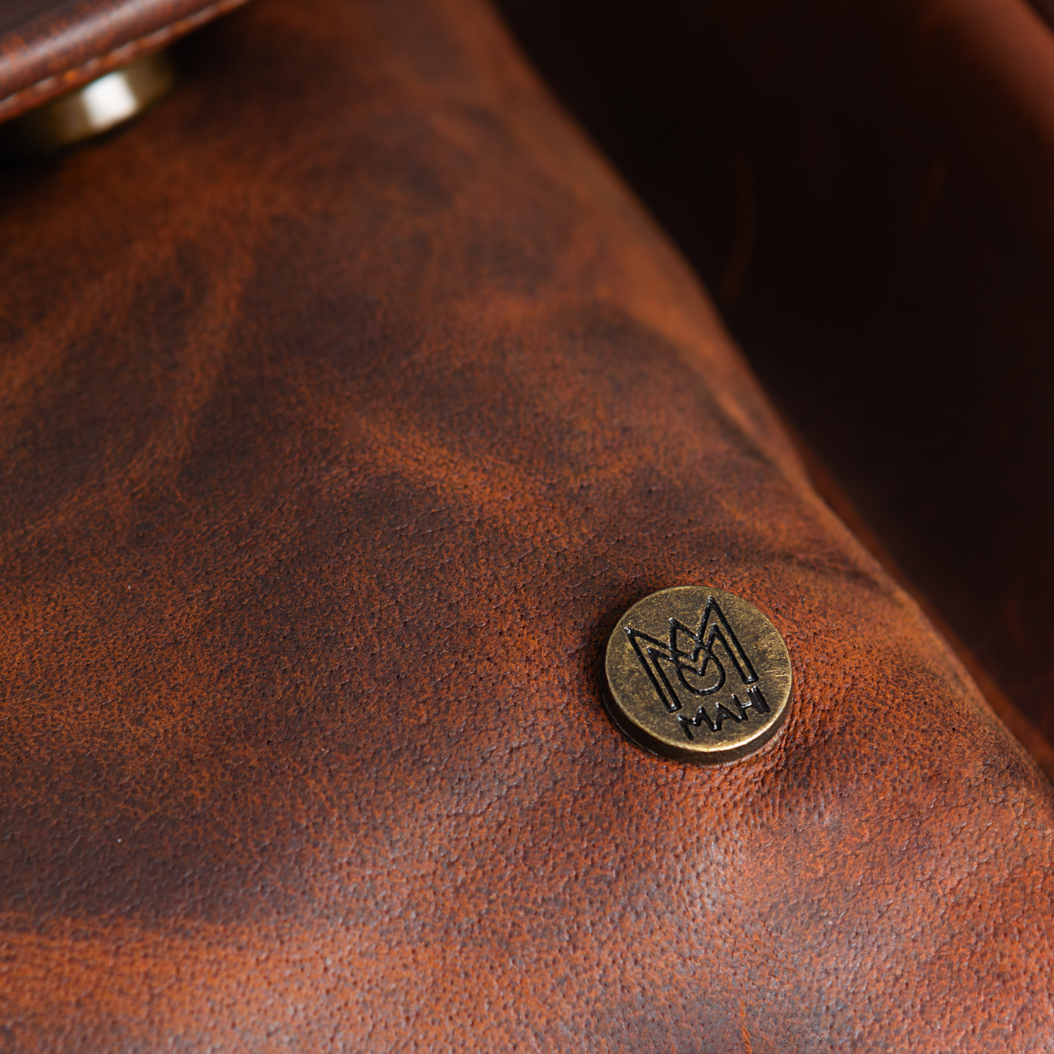 Close-up of a metal logo badge and textured waxy brown leather