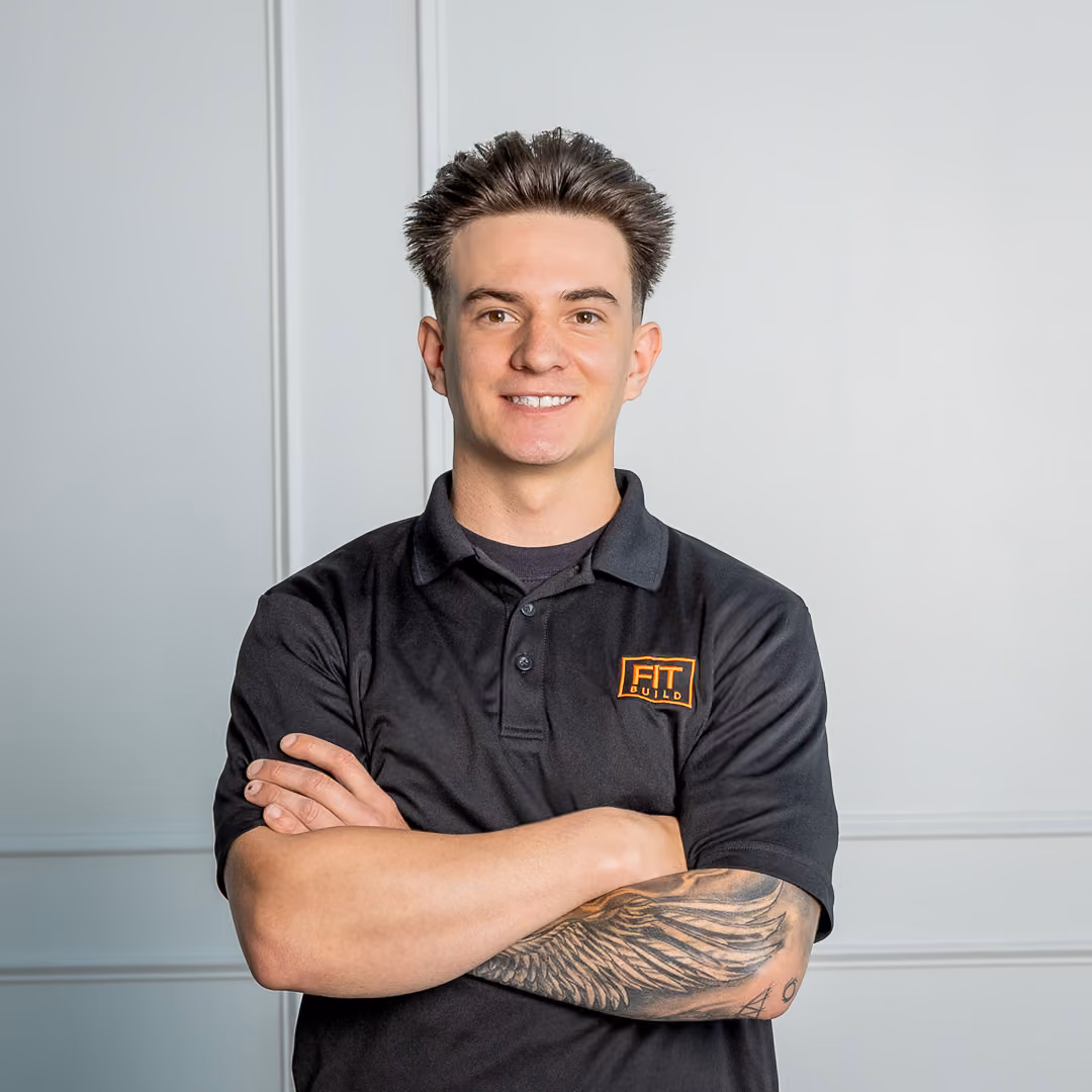 Smiling young man with crossed arms and wing tattoo wearing a black shirt with FIT Build logo.