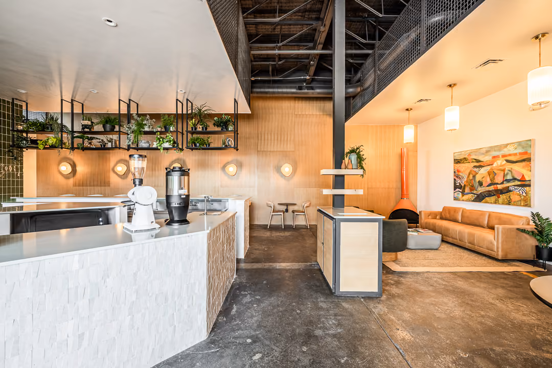 Modern lobby with white reception desk, hanging plants, wooden wall, and seating area with a couch and artwork.
