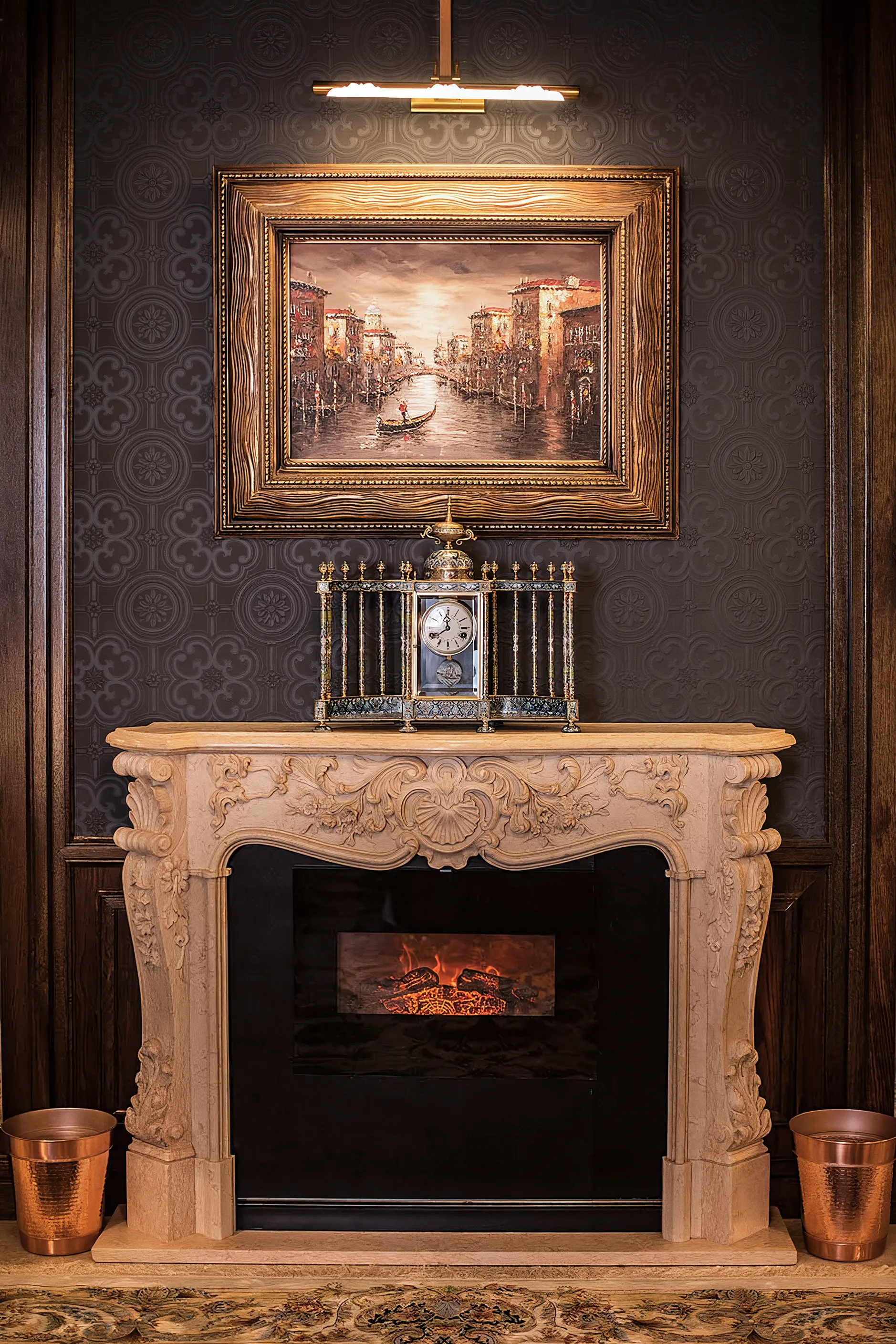 Traditional marble fireplace with original painting and brass trash baskets. An old school clock is placed on the fireplace. with gray modern 3d wall paper