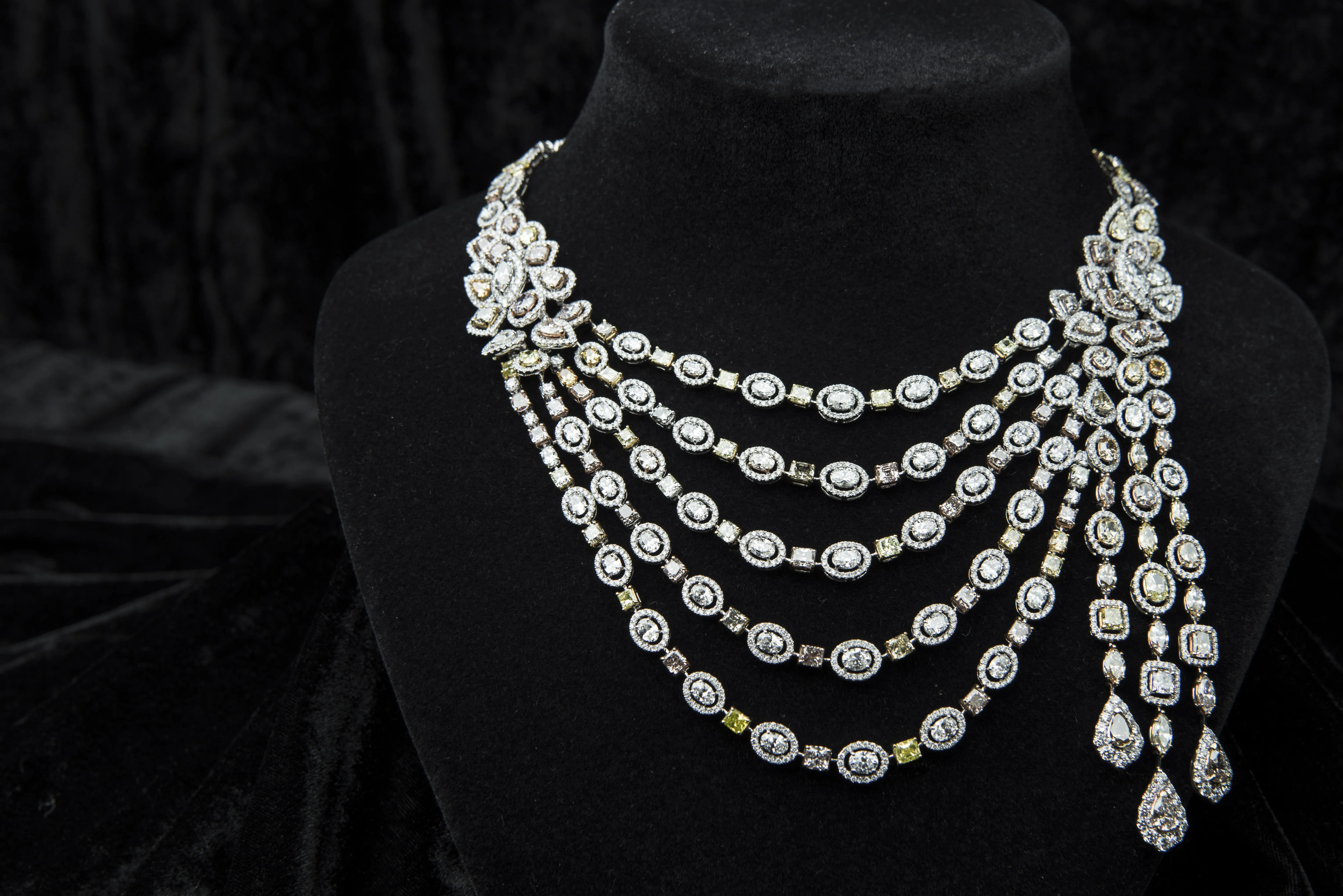 A moody shot of a diamond necklace on a black display holder and a black velvet background. 