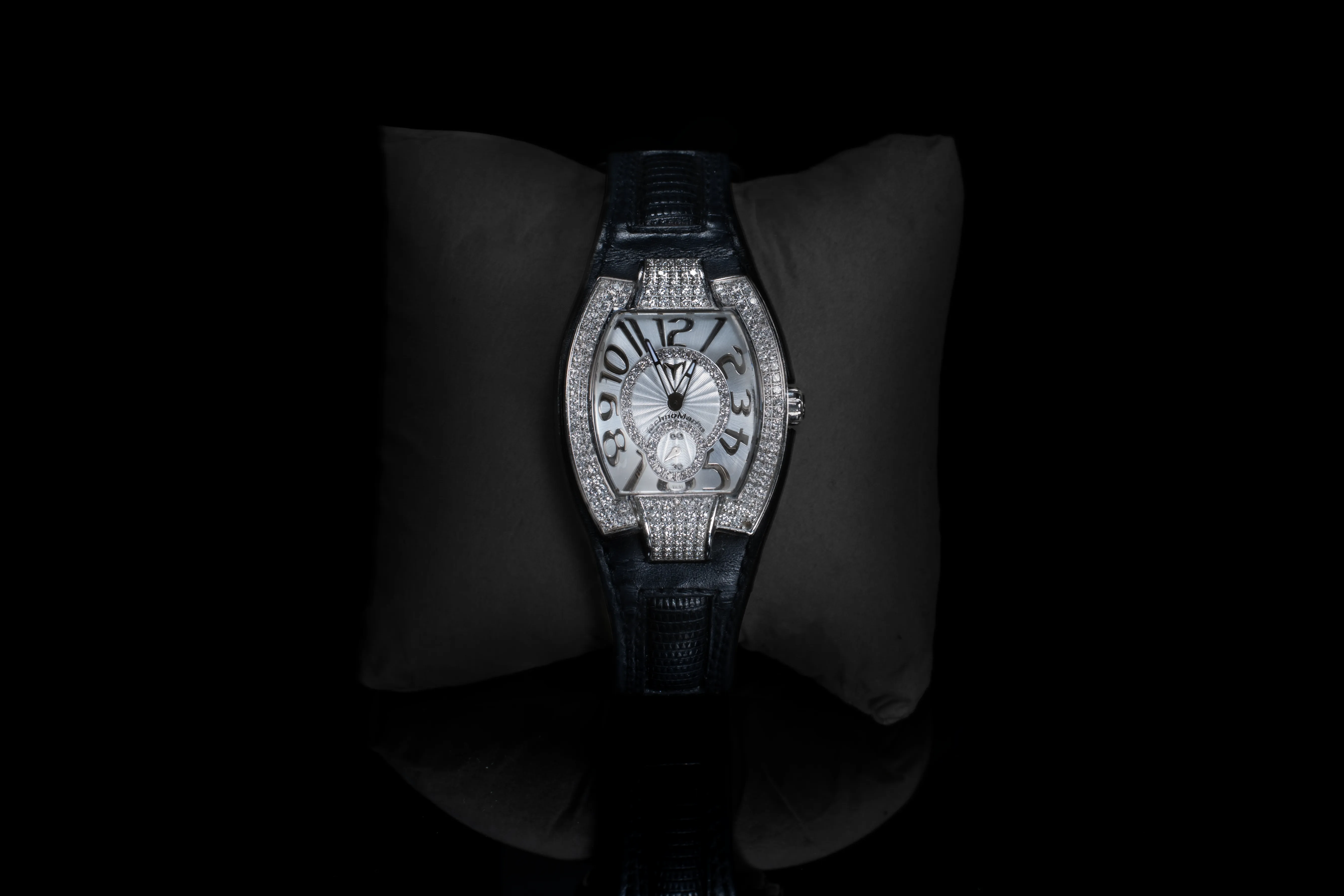 A moody shot of a luxury watch with diamond details and a blue genuine leather strap. On black reflective glass surface. 