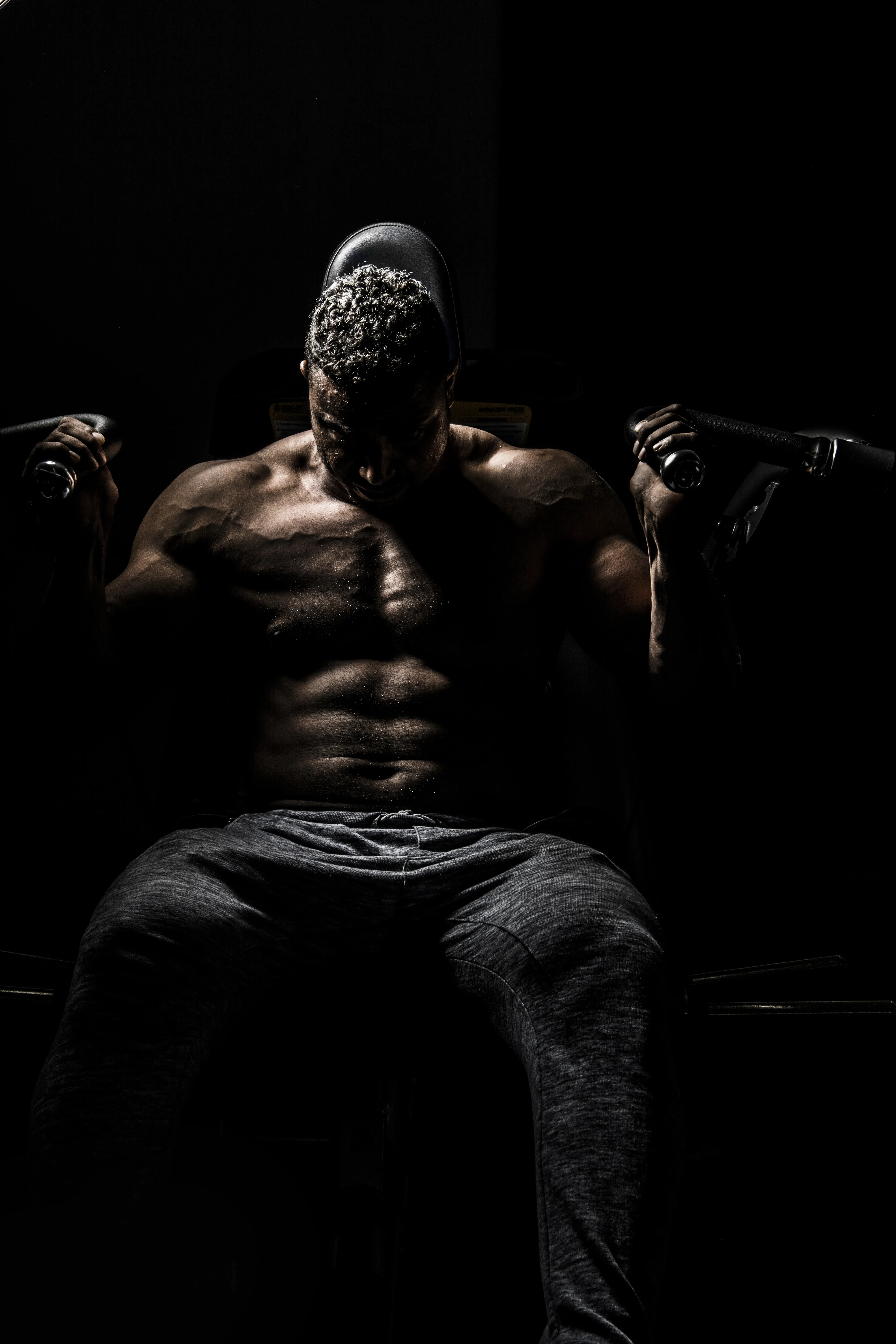 A silhouette of a bodybuilder lifting, shirtless, wearing black jeans. Visible abs and traps.
