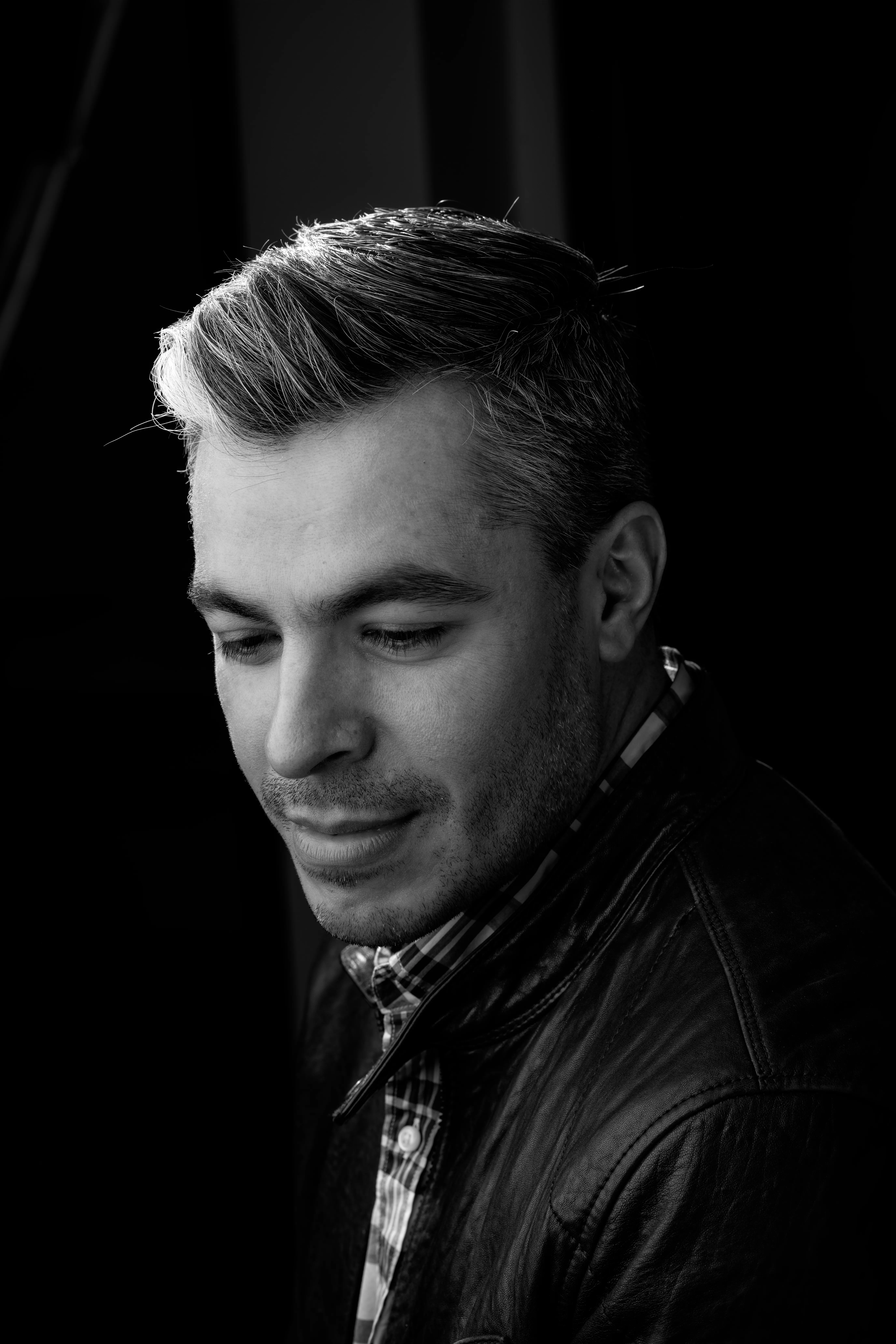 Black and white portrait of a handsome man with salt-and-pepper hair. Wearing a leather jacket and a white shirt. 