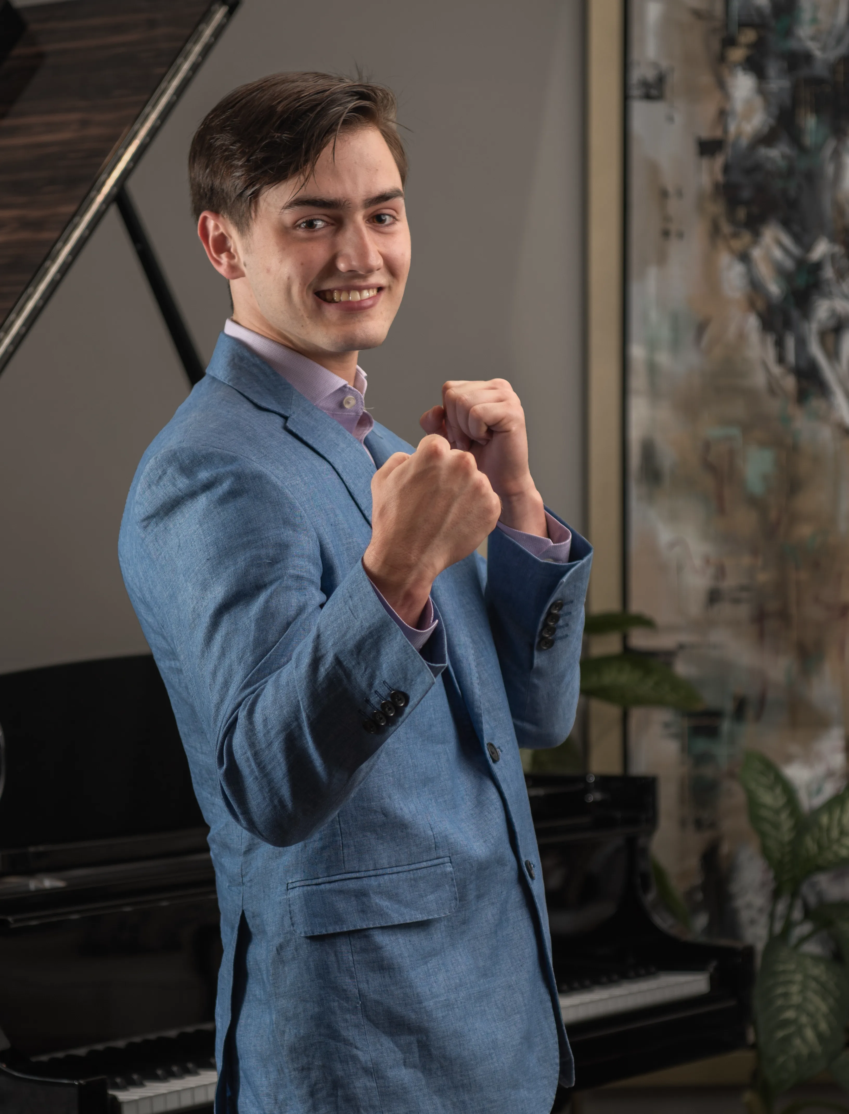 LinkedIn profile photo of a young man wearing a suit, taking a strong pose, with modern painting and a black Stanley piano in the background.