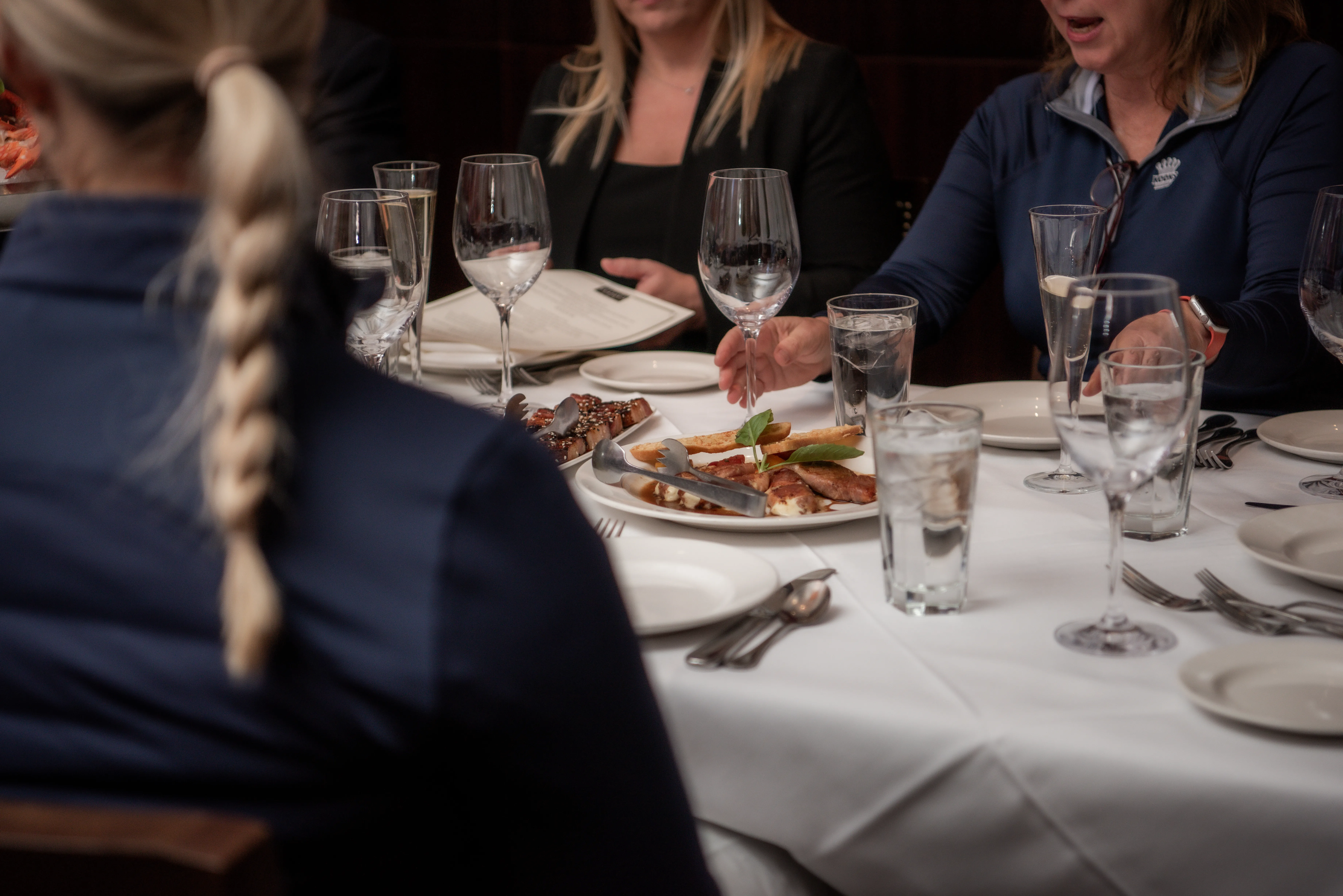 High-profile business dinner; guests are seated. Dinner is served on a white tablecloth.