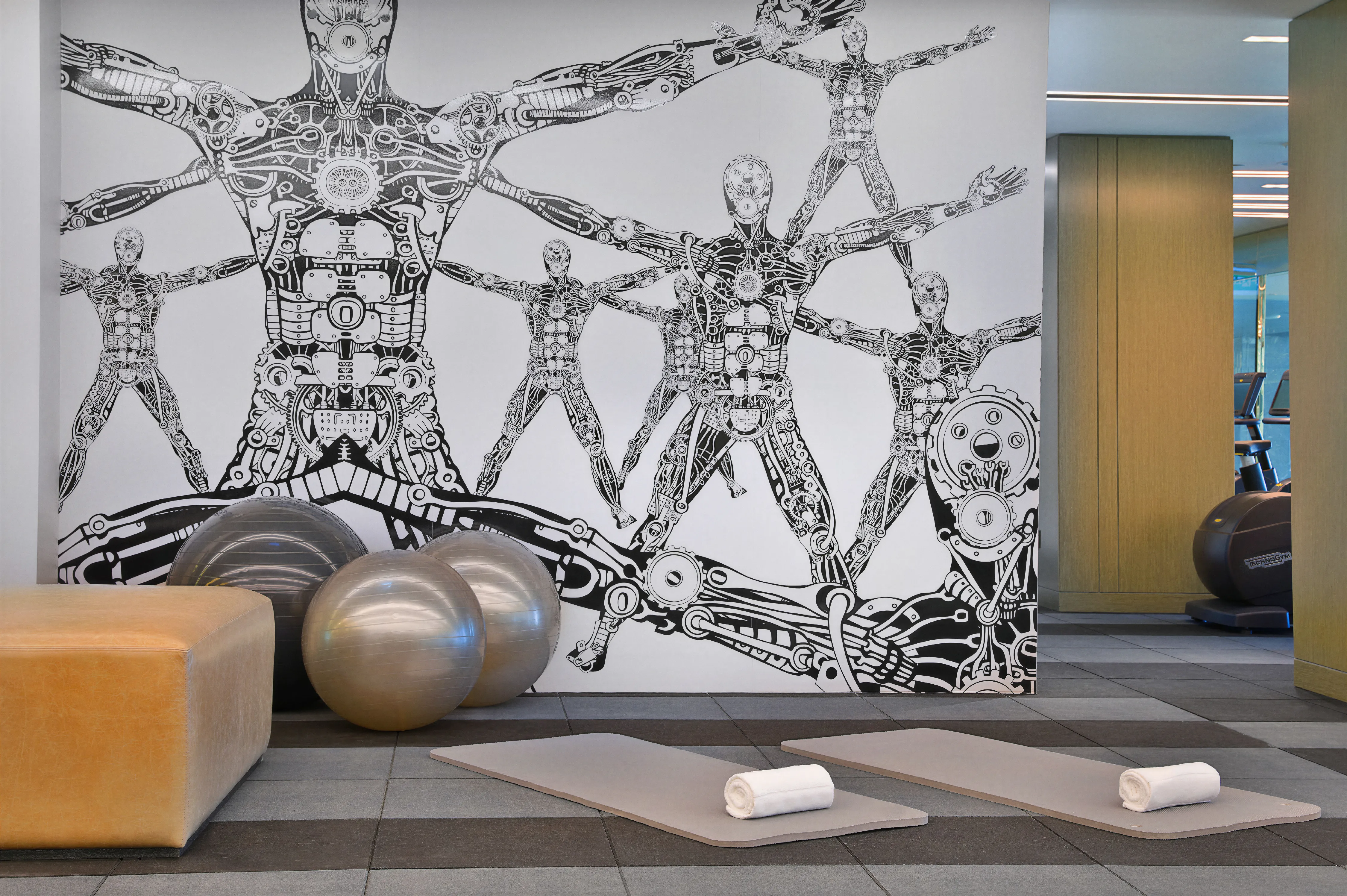 Modern gym interior, featuring digital black-and-white full-wall art of a mechanical human. 