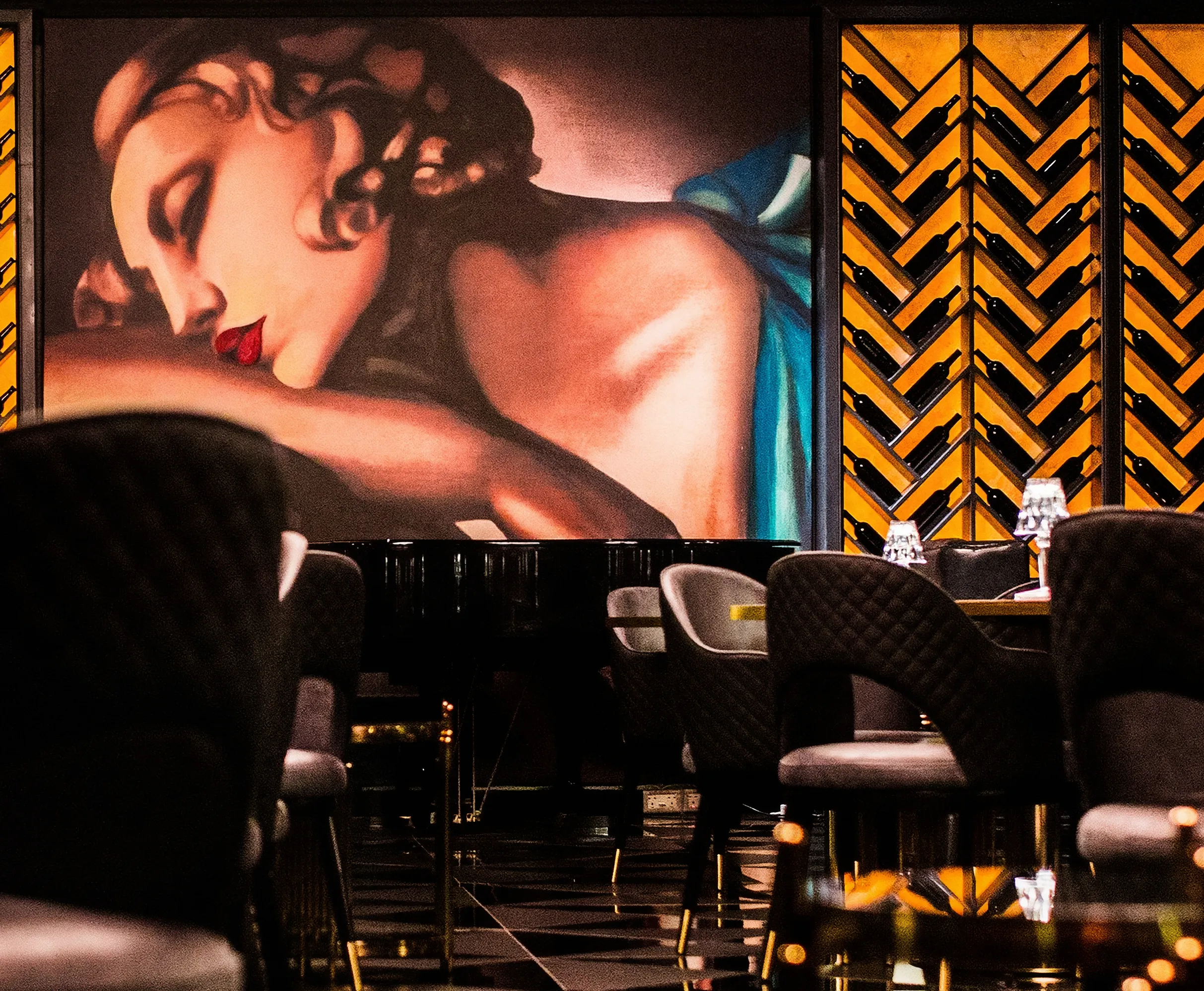 Luxury cigar lounge and bar, with leather Bentley-style chairs, custom multi-finish black floor, and Art Deco center wall. Backlit onyx wine shelves. 