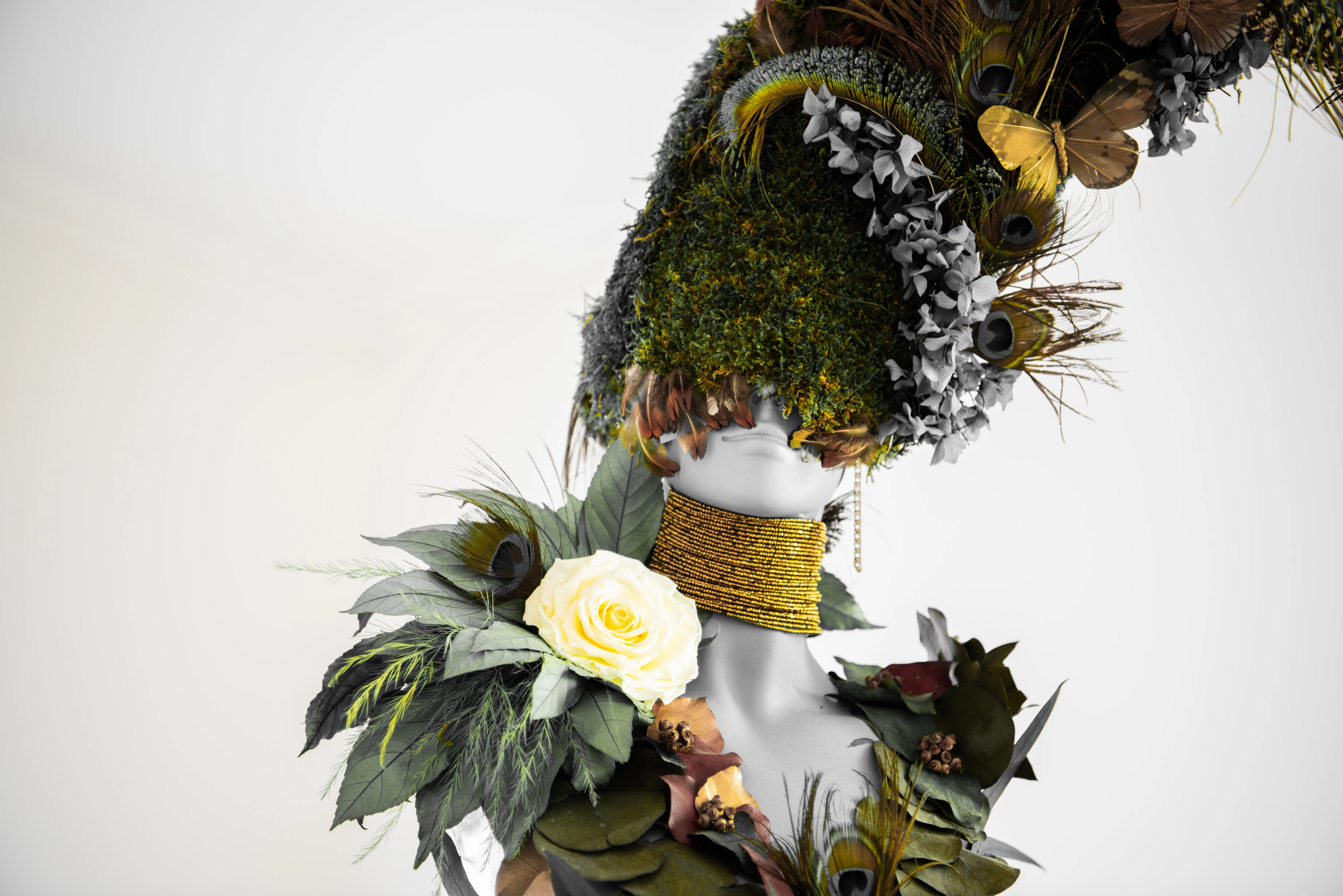 Custom multimedia sculpture of a woman.  Her hair is made of sustainable greenery, and her dress is made of leaves and flowers. Wearing a gold necklace. 