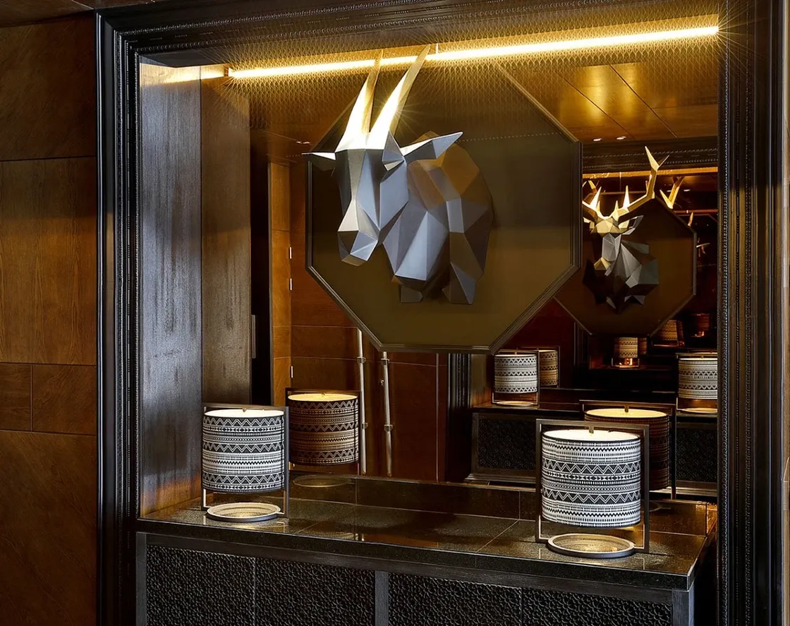 Hotel interior featuring a fractal animal-head wall sculpture in black and gold on a mirror wall, over a custom metal-and-fabric console and black-and-white table lamps. 